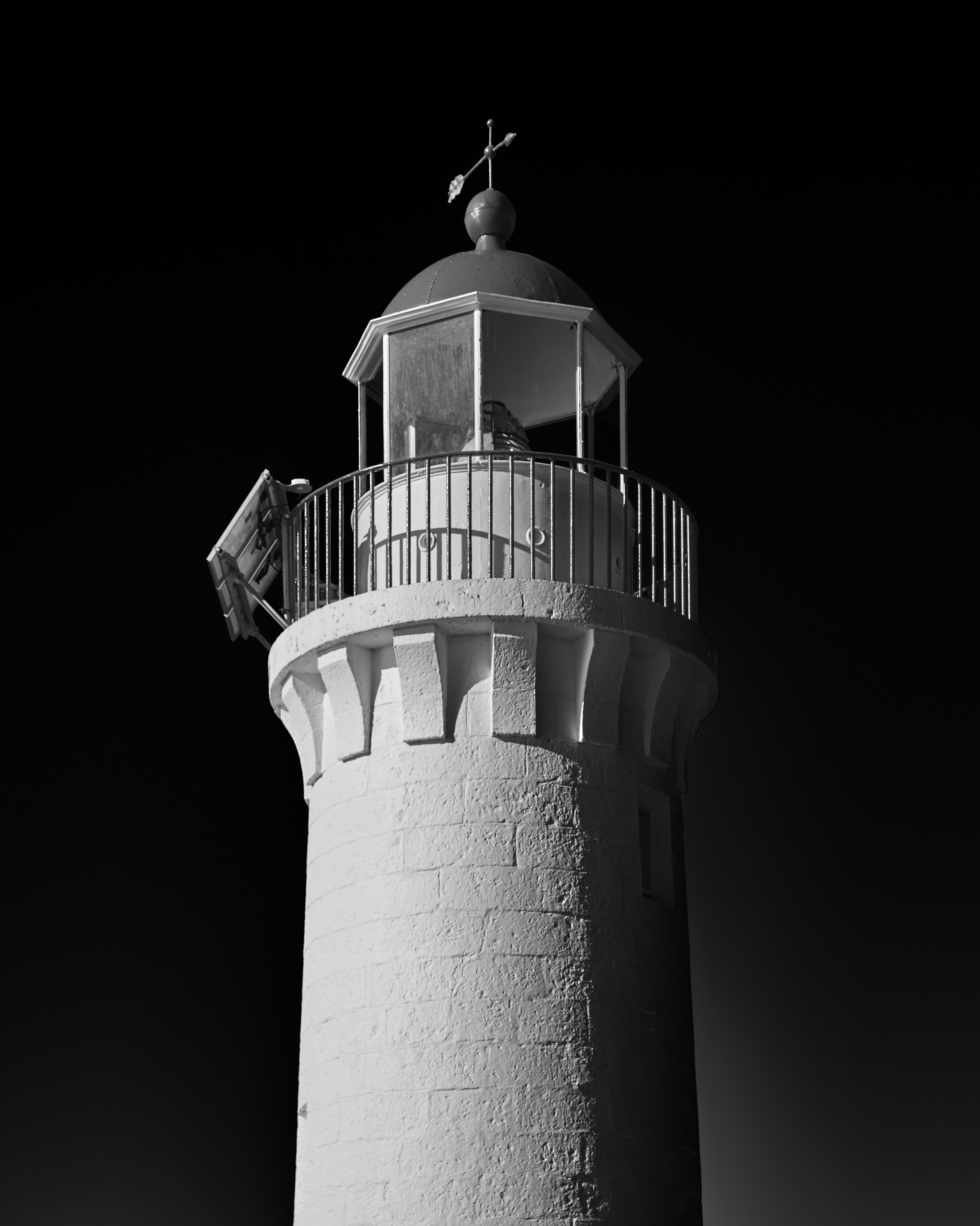 A stone lighthouse tower with a metal lantern room against a black sky.