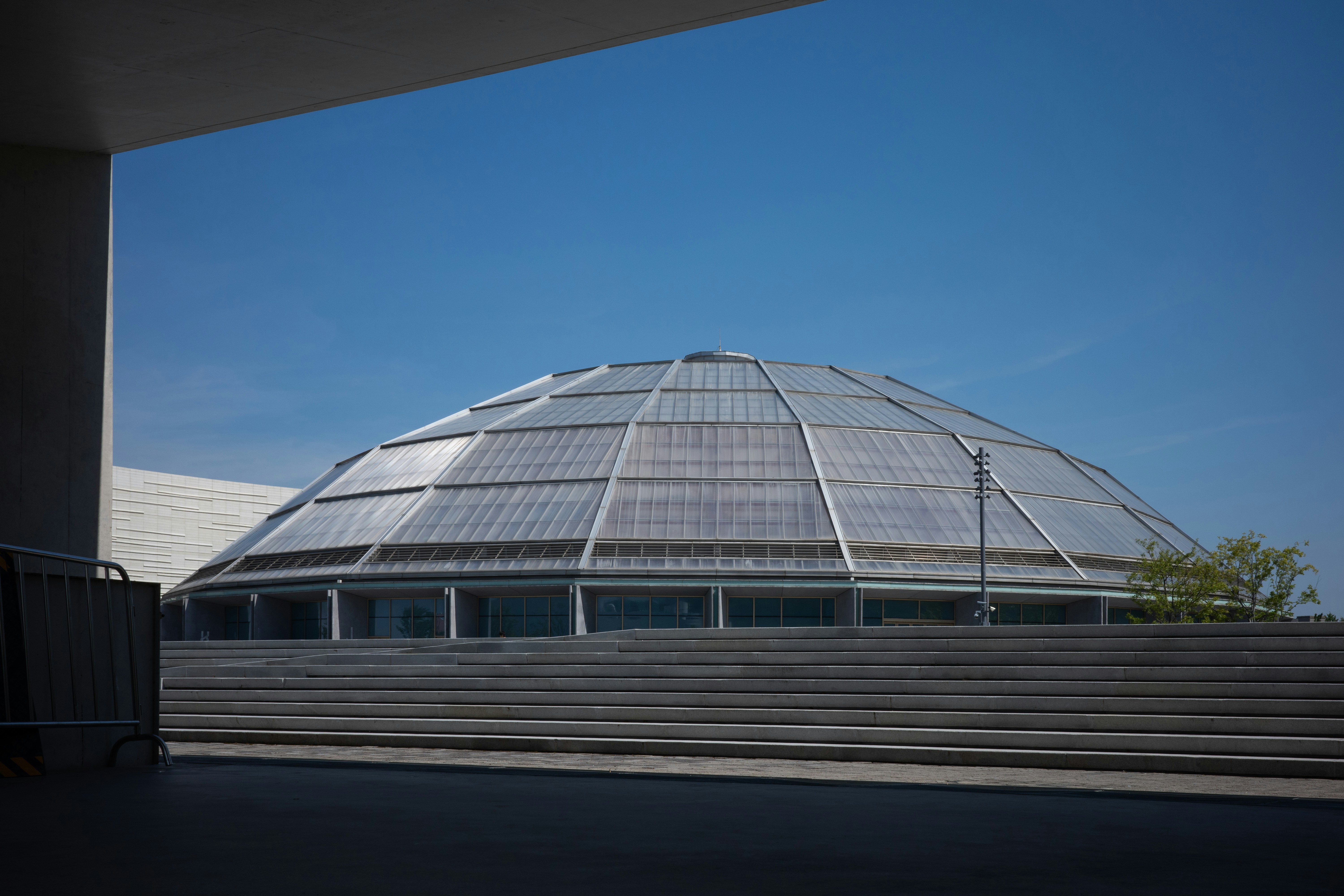 A large glass dome building behind wide concrete steps under a clear blue sky.