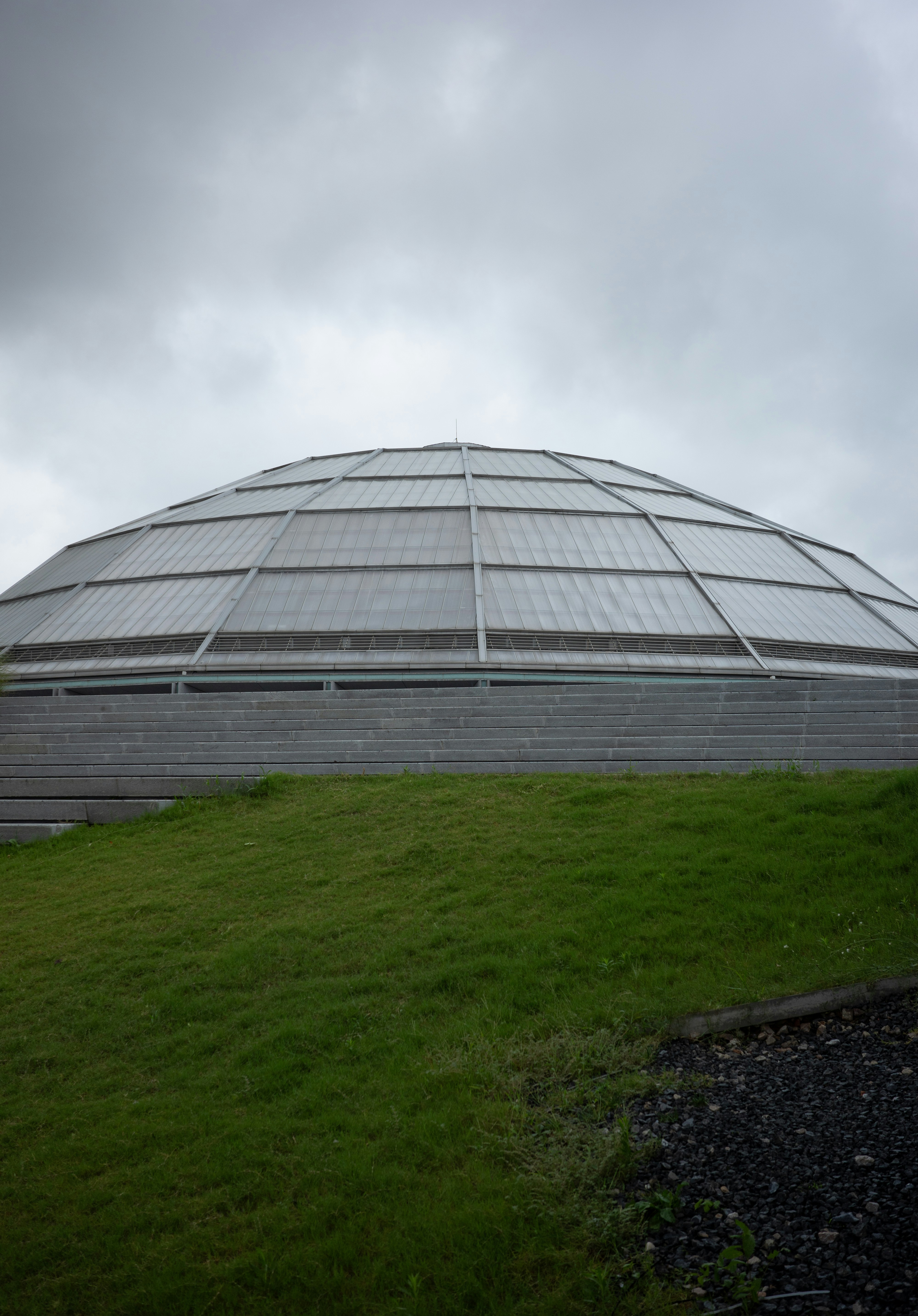 A large glass dome building above concrete steps and a grassy hill.