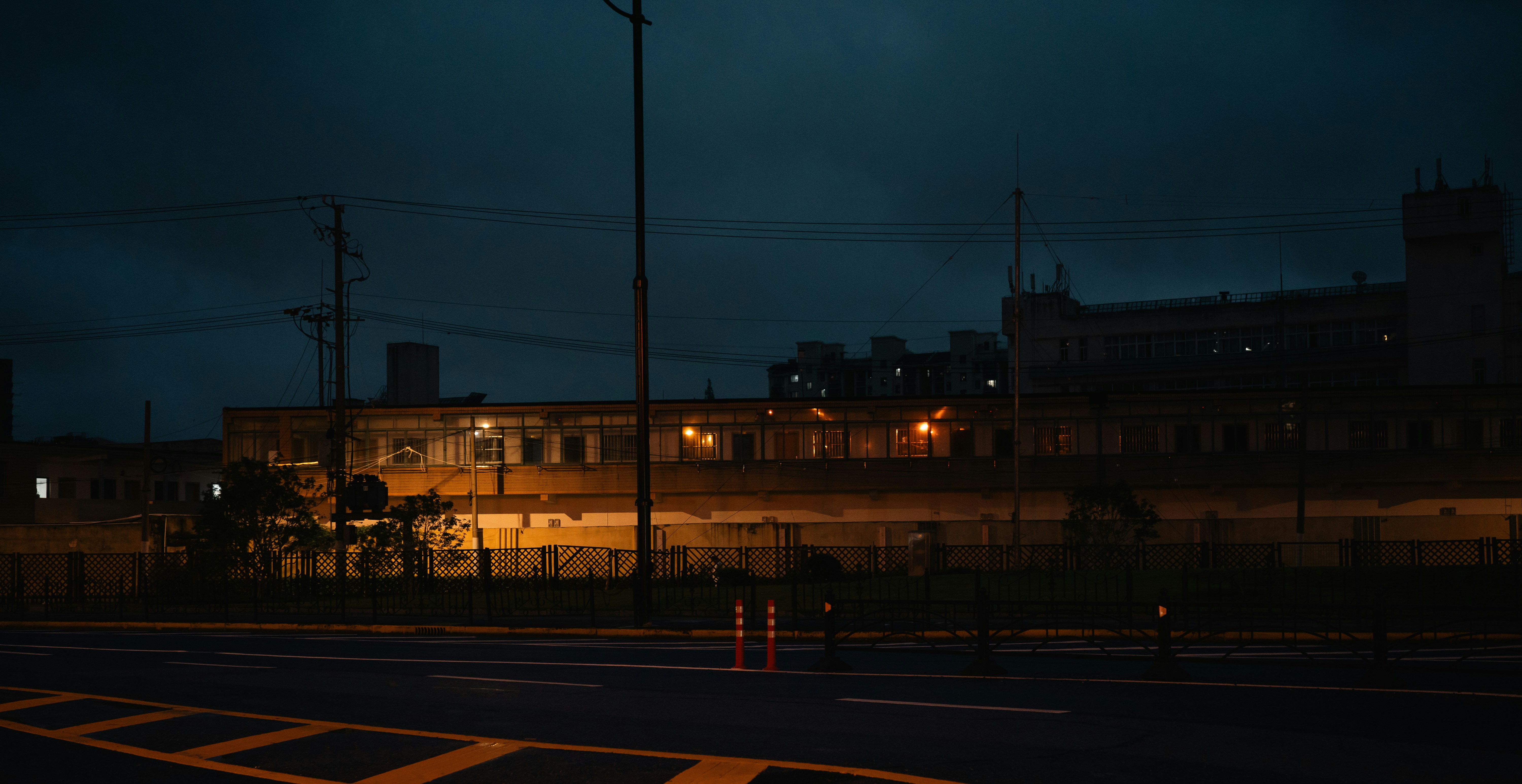 A dark street at night with a long building illuminated by warm interior lights.