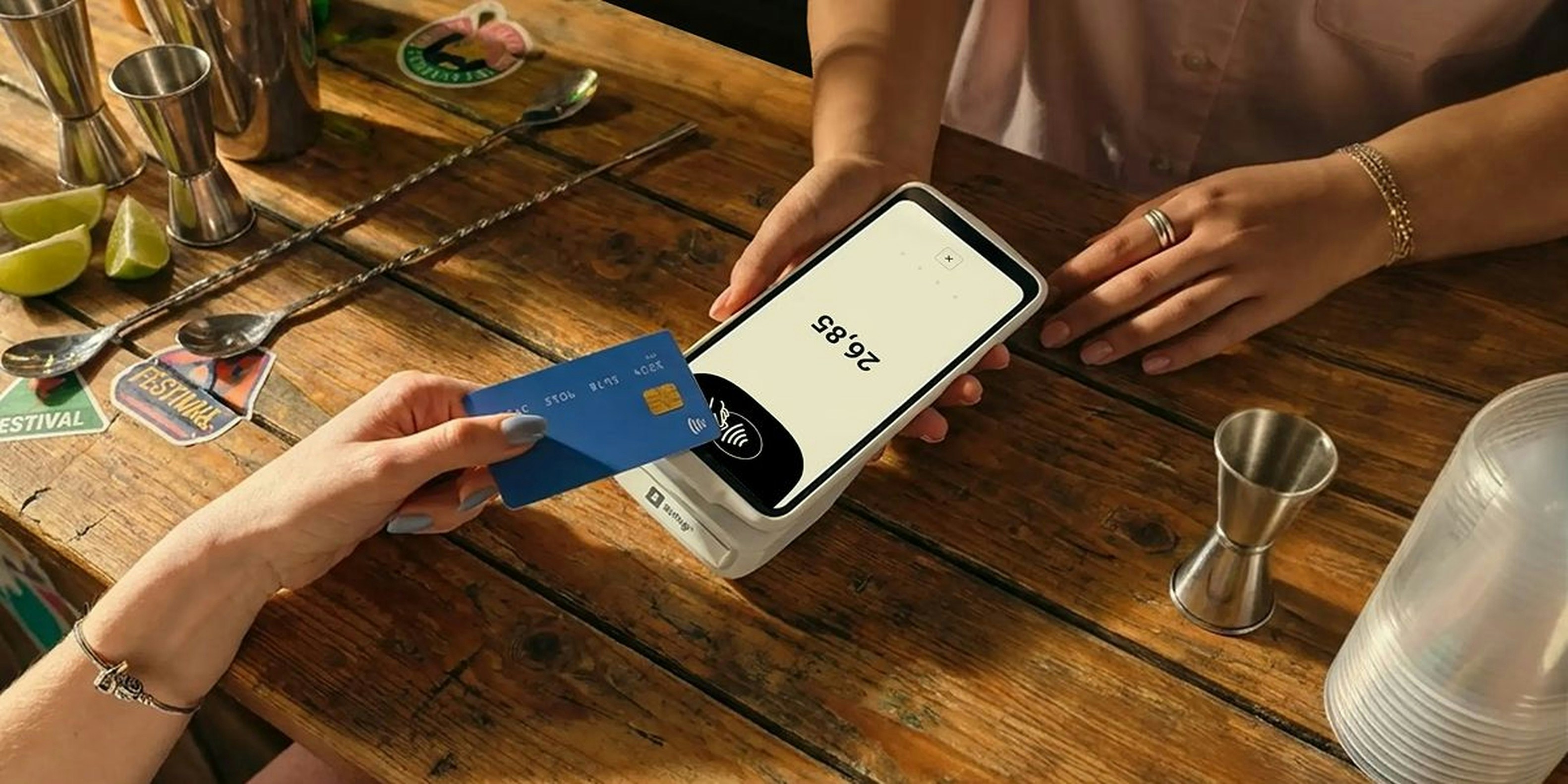 A person tapping a blue credit card on a payment terminal on a wooden counter