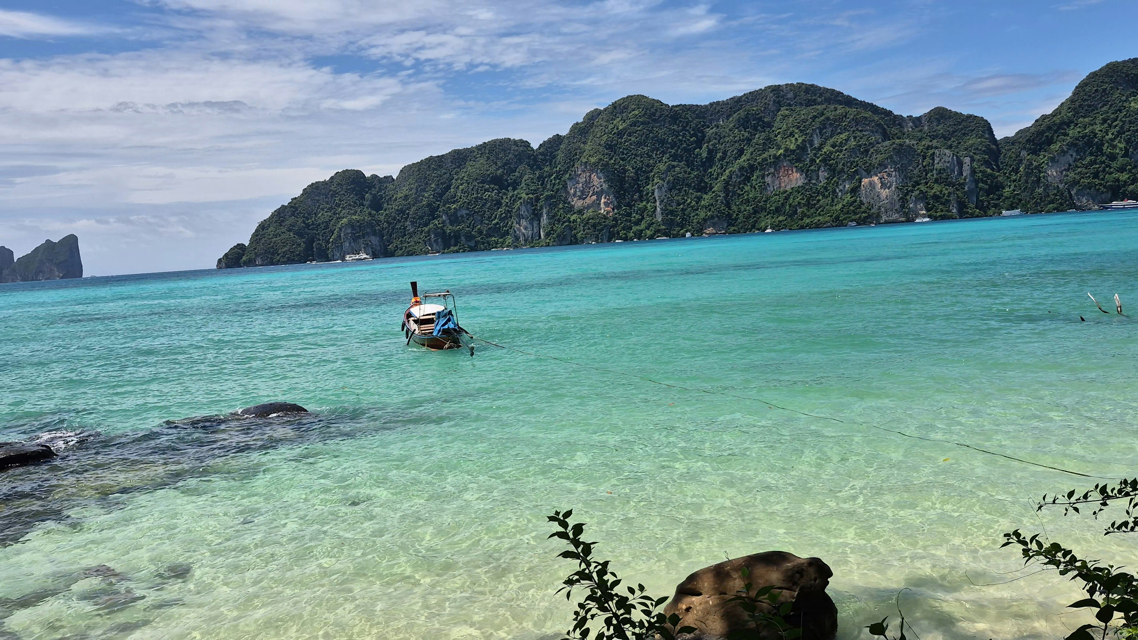 A long-tail boat floating in clear turquoise water near limestone cliffs in Thailand