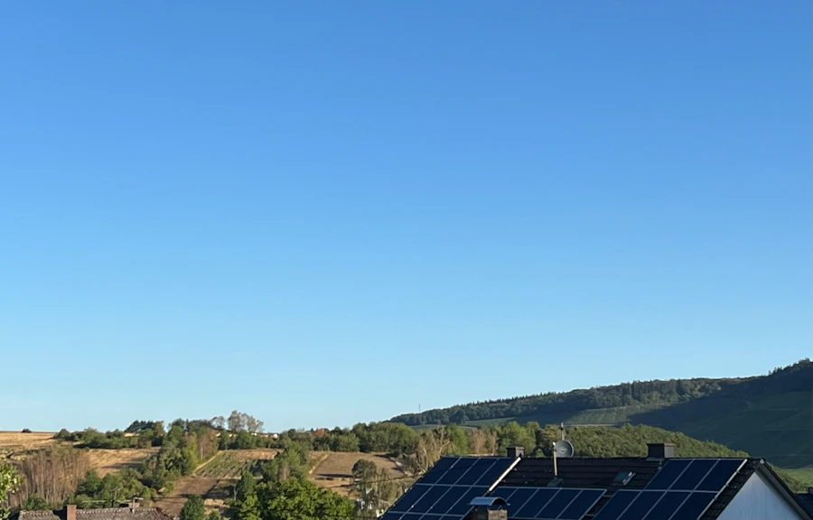 青空と緑の丘を背景にした屋根上の太陽光パネル