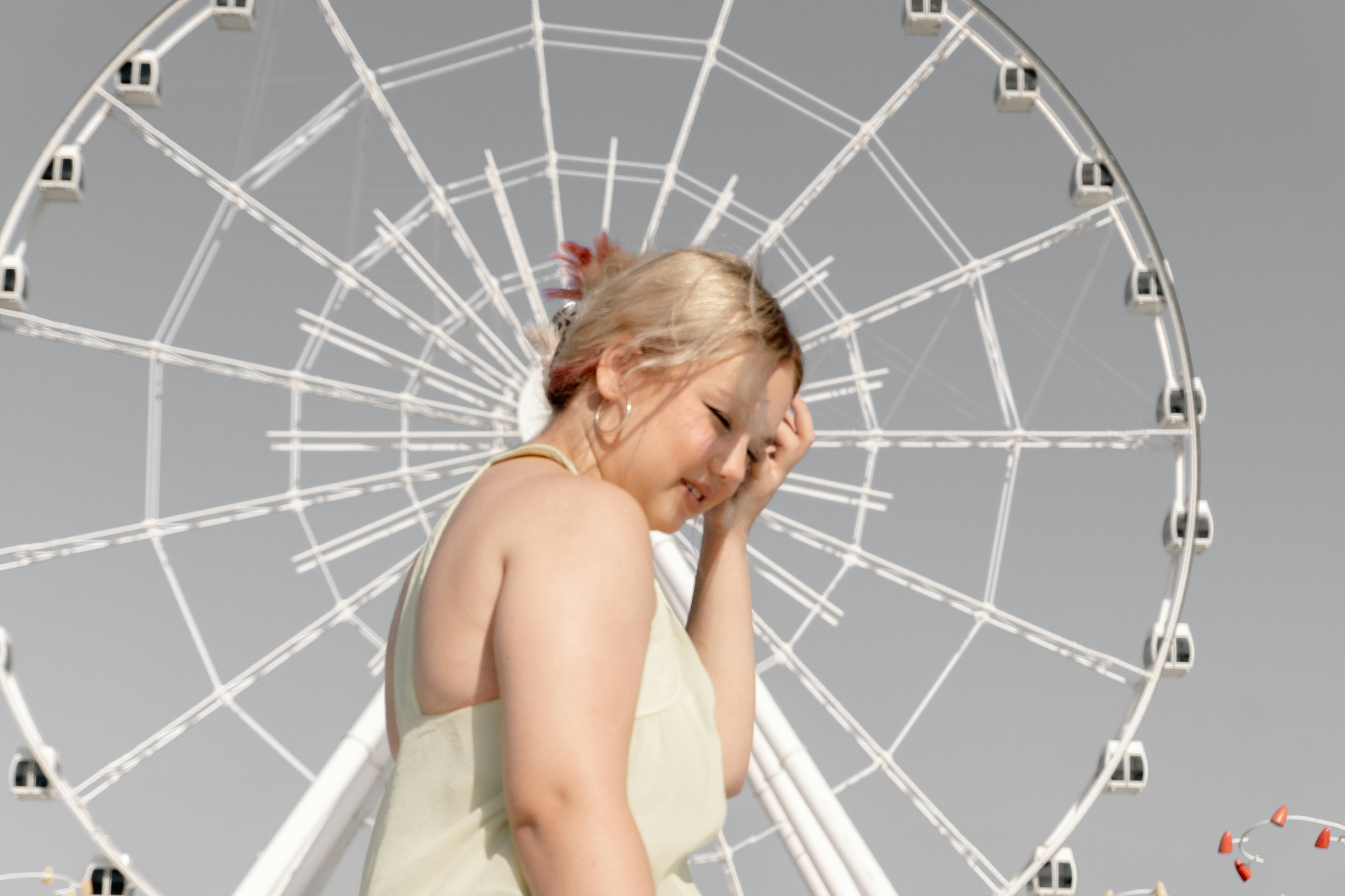 A woman with blonde hair touching her head in front of a ferris wheel