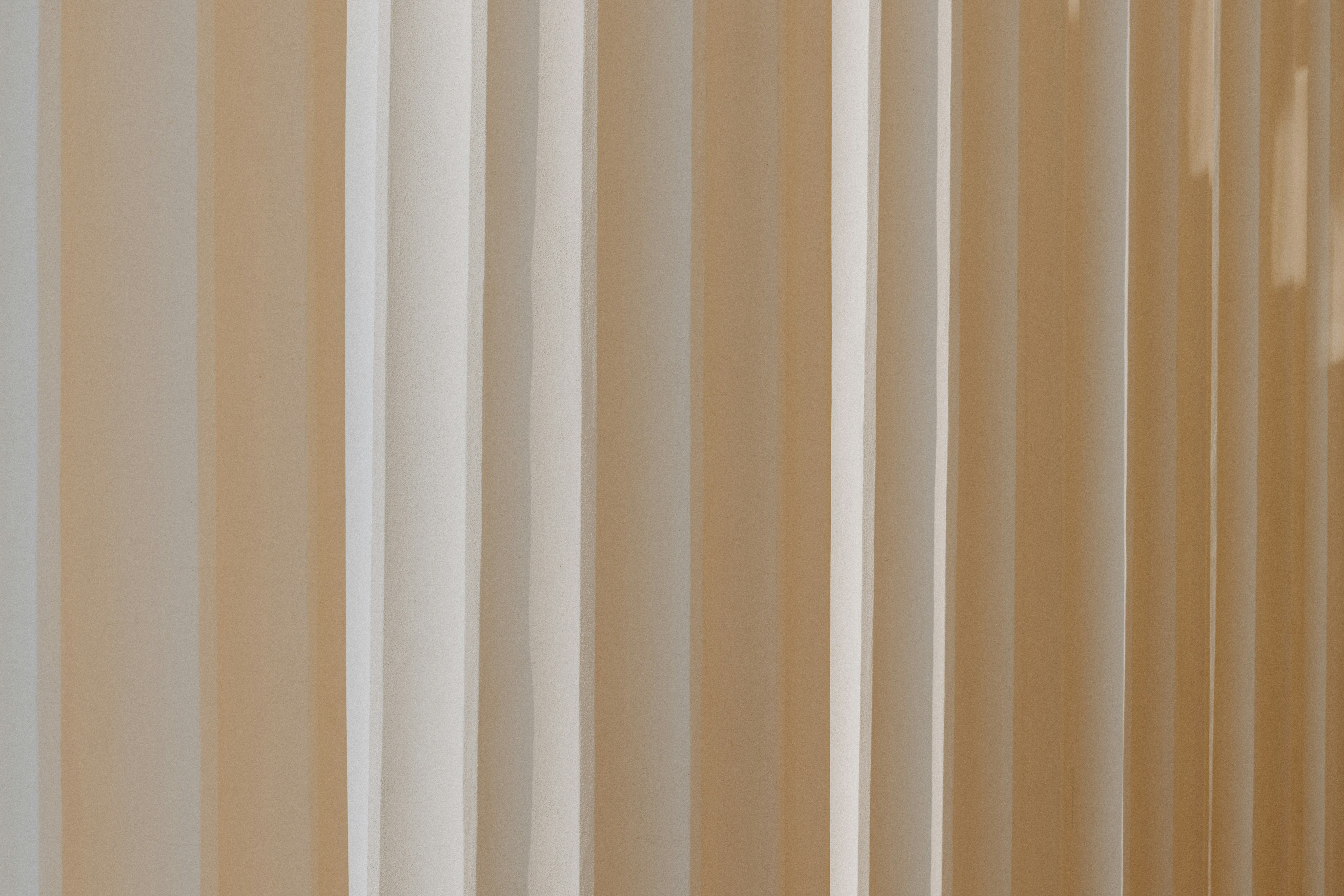 Vertical beige and white stripes with soft shadows on a textured surface.