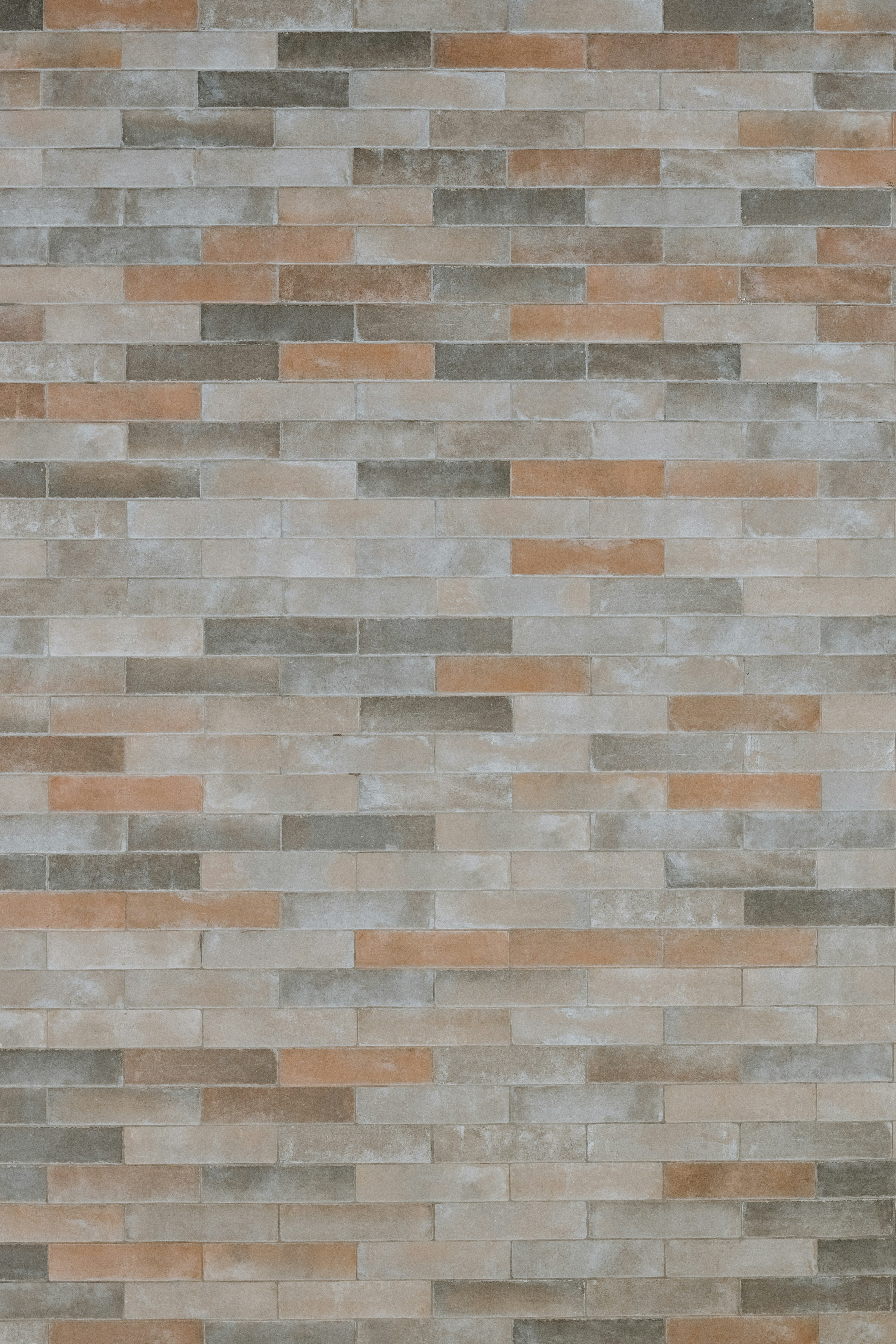 A wall of rectangular bricks in shades of grey, beige, and terracotta.