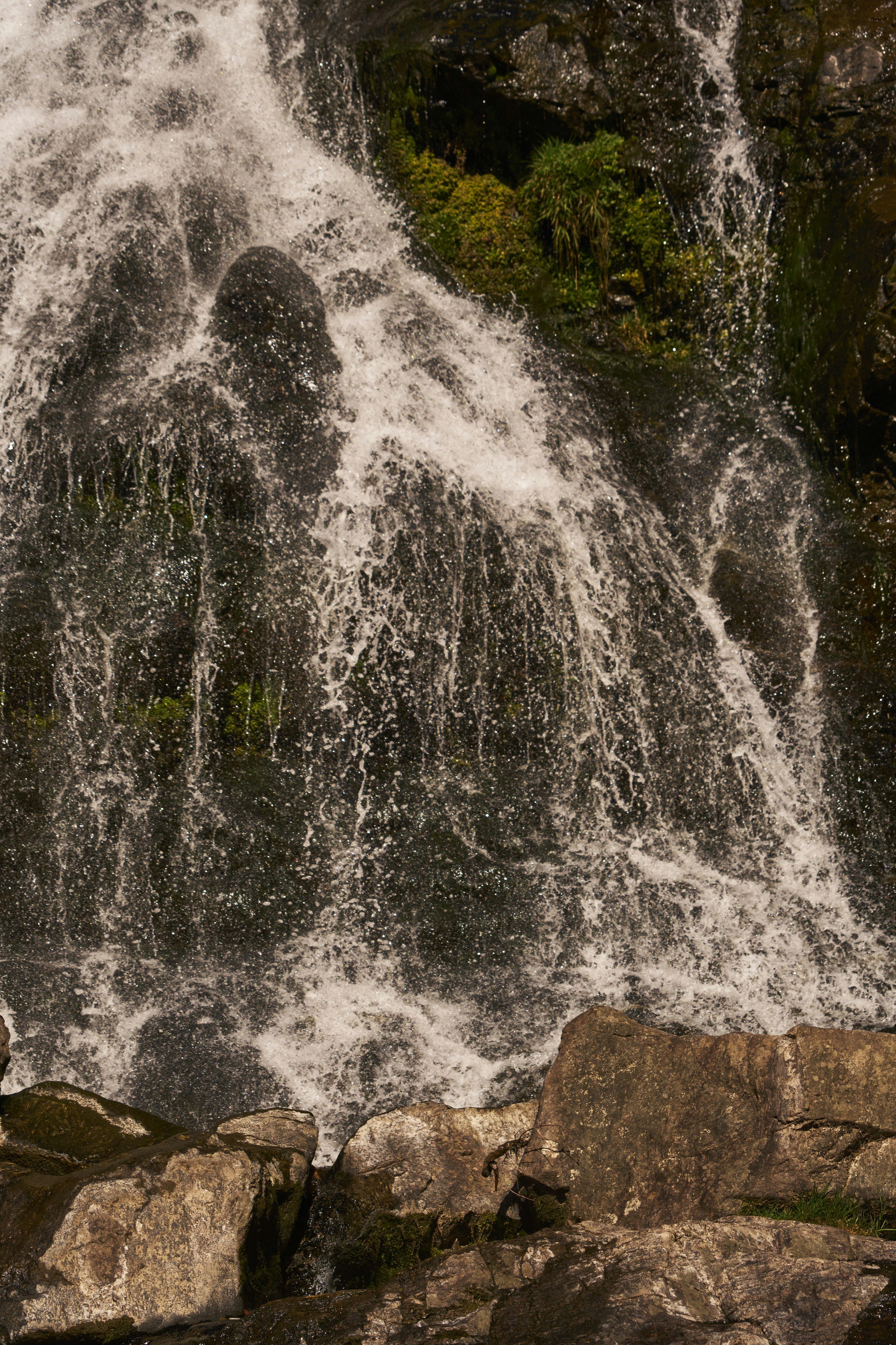 Water cascading over dark mossy rocks into a pool below.