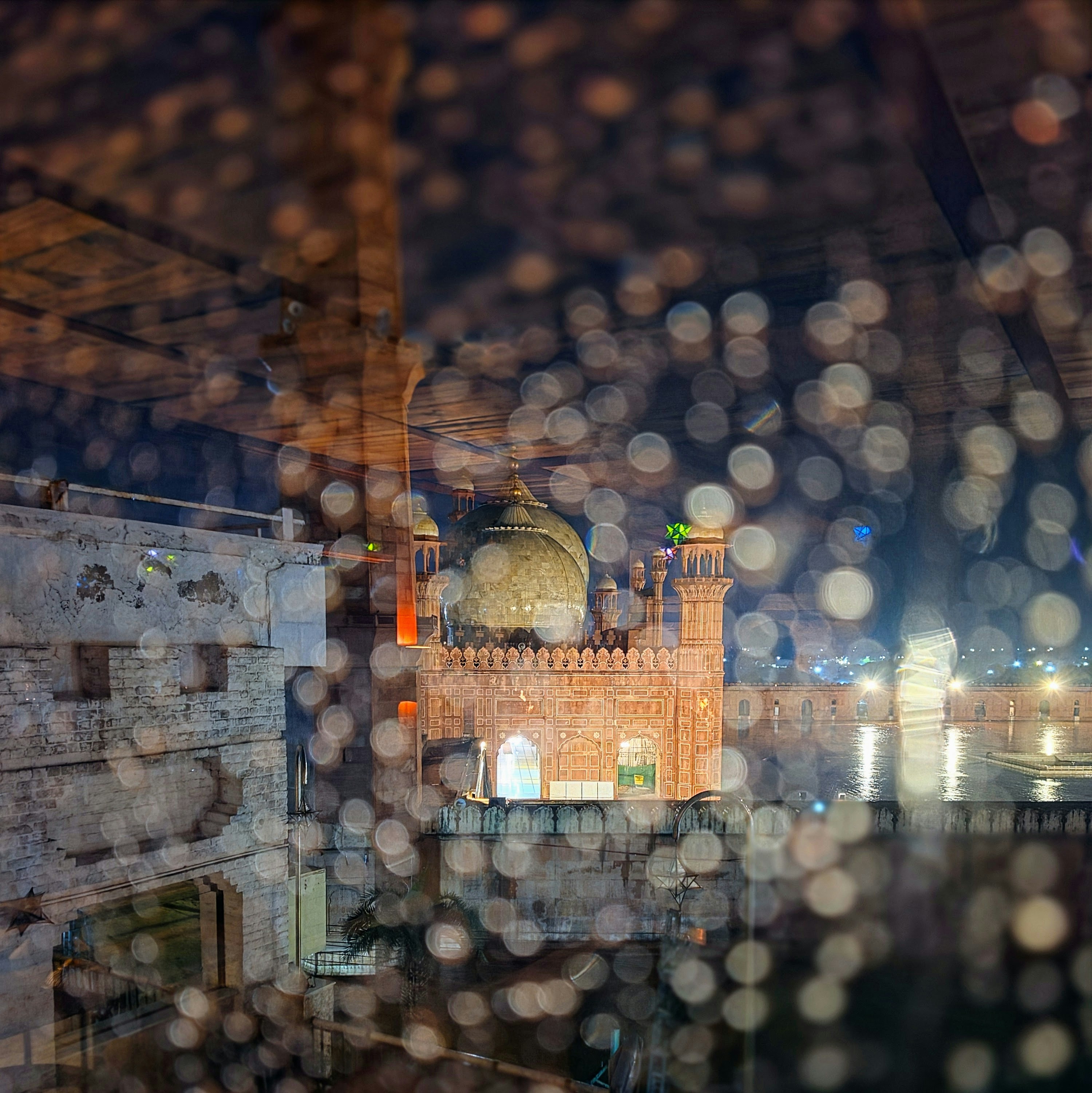 The Badshahi Mosque in Lahore viewed through a rain-streaked window at night.