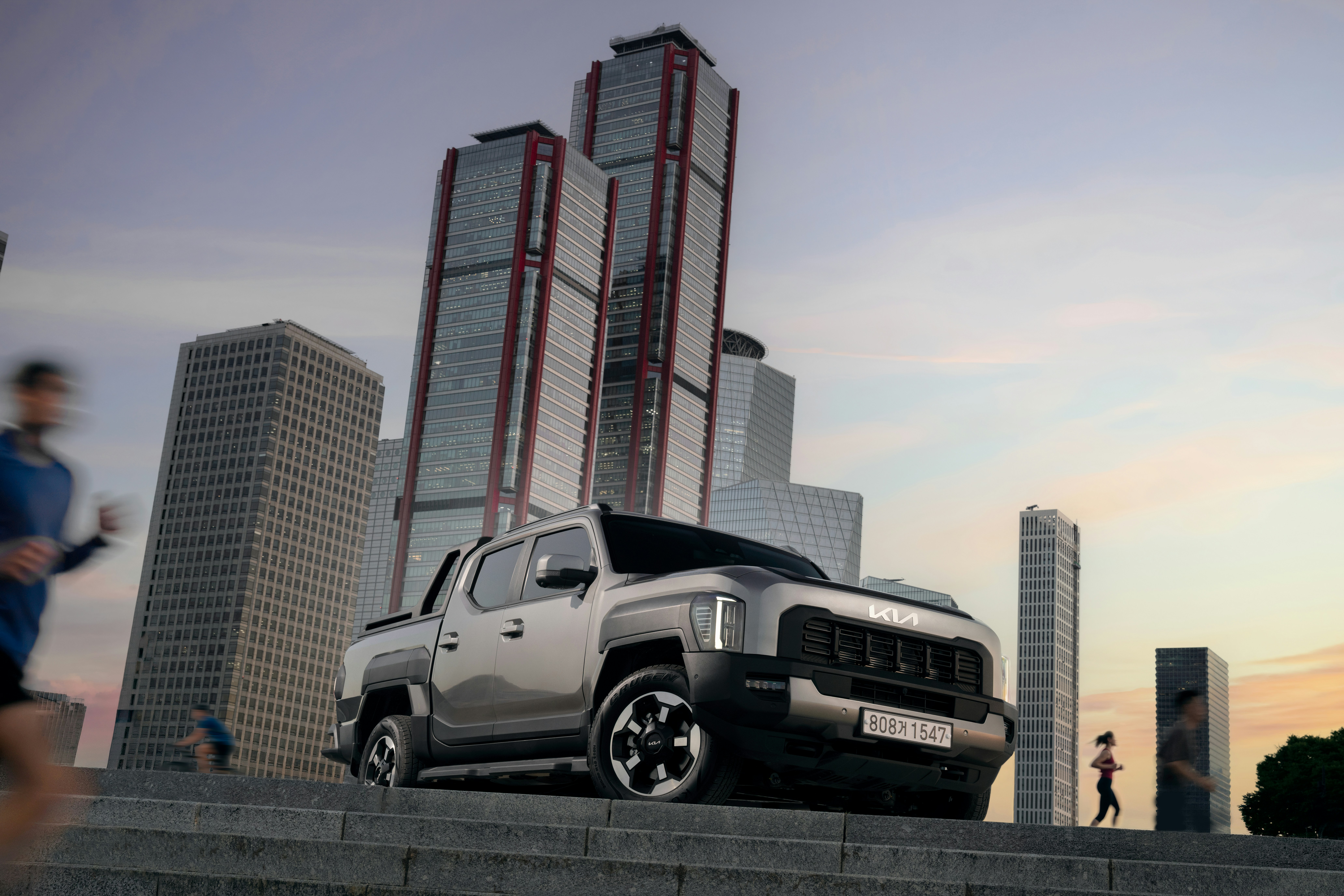 A silver Kia pickup truck parked on stone steps before modern city skyscrapers