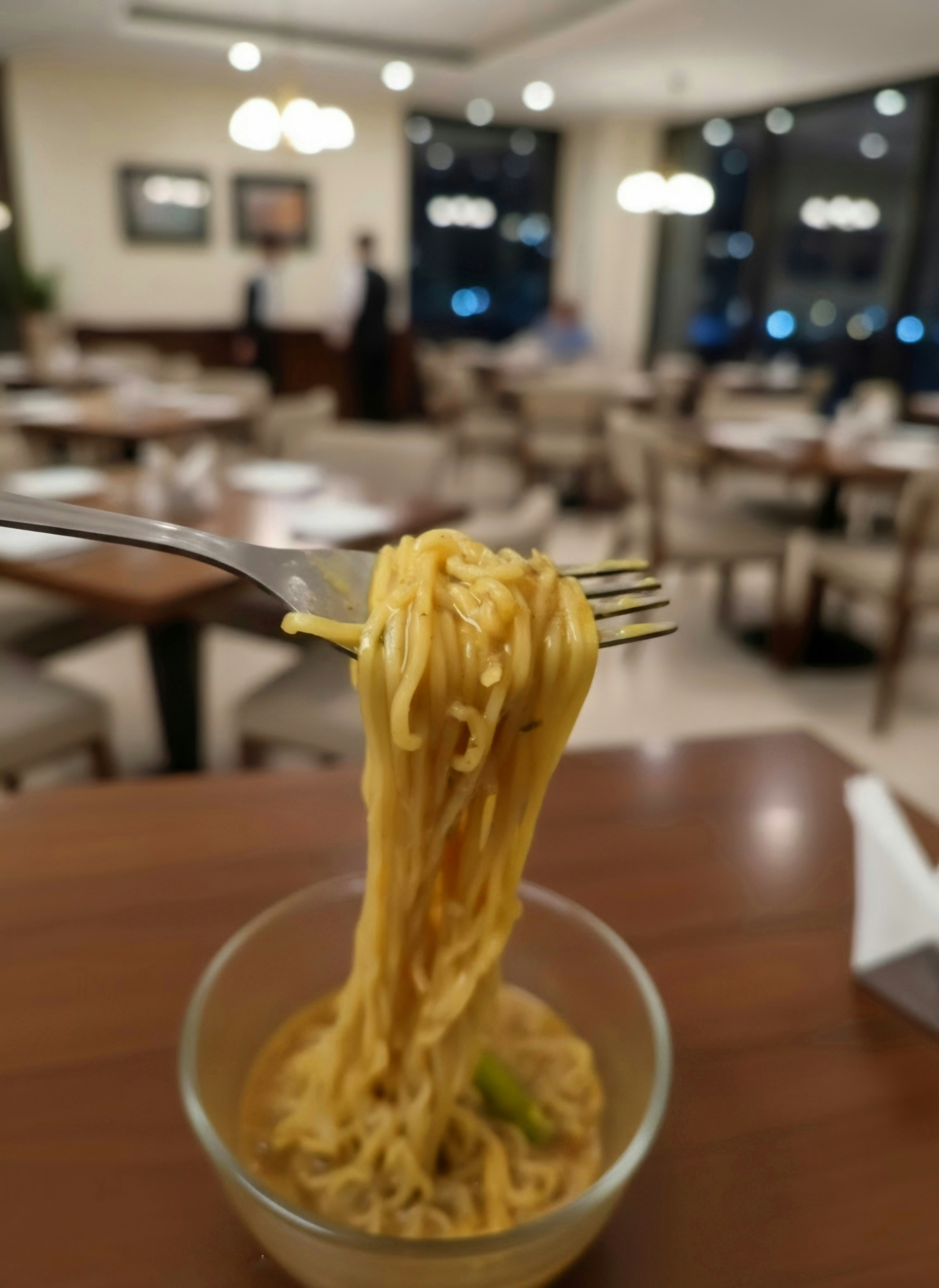 Sebuah garpu mengangkat mie dari mangkuk kaca di ruang makan restoran