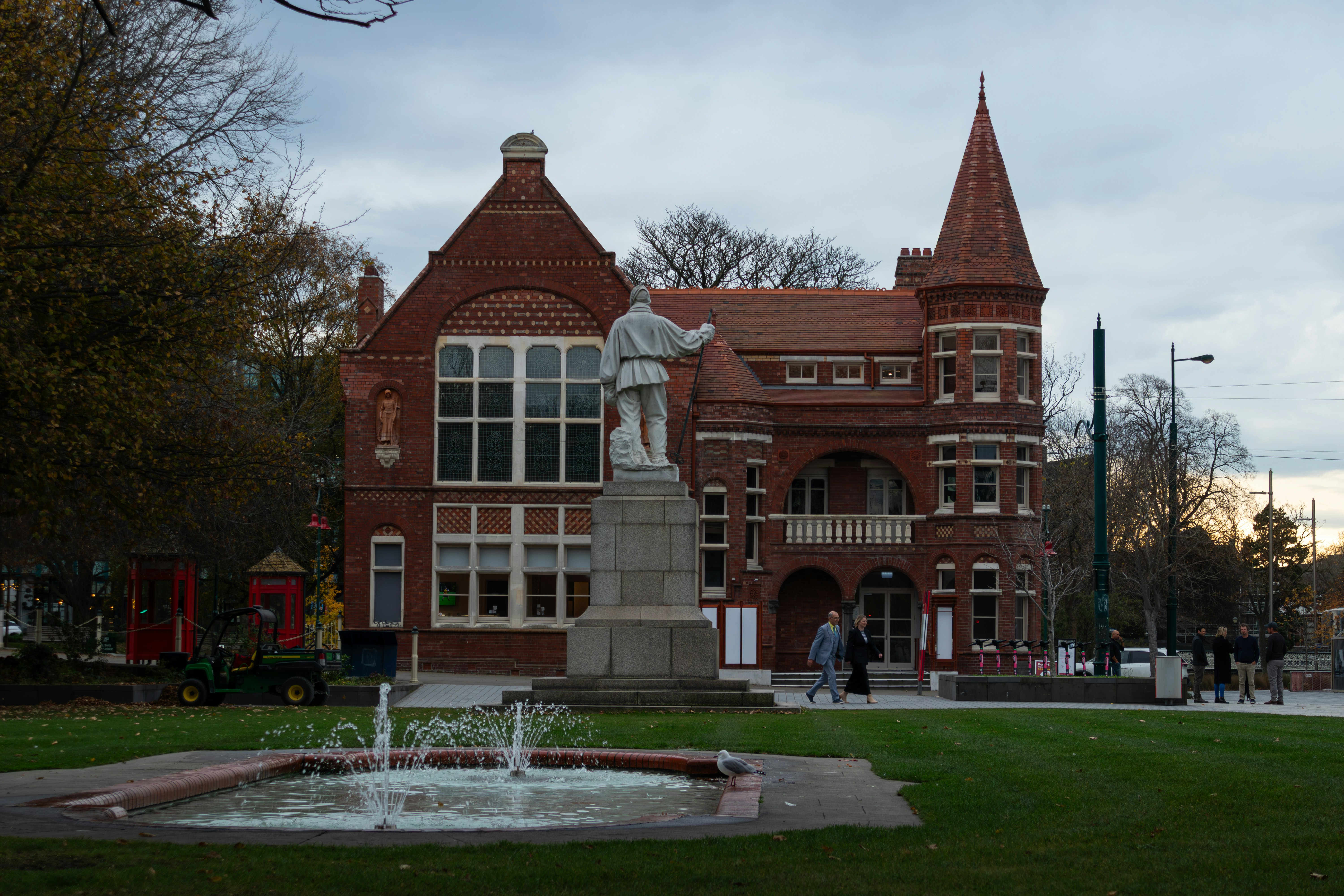 A stone statue of a man in a park before a red brick building