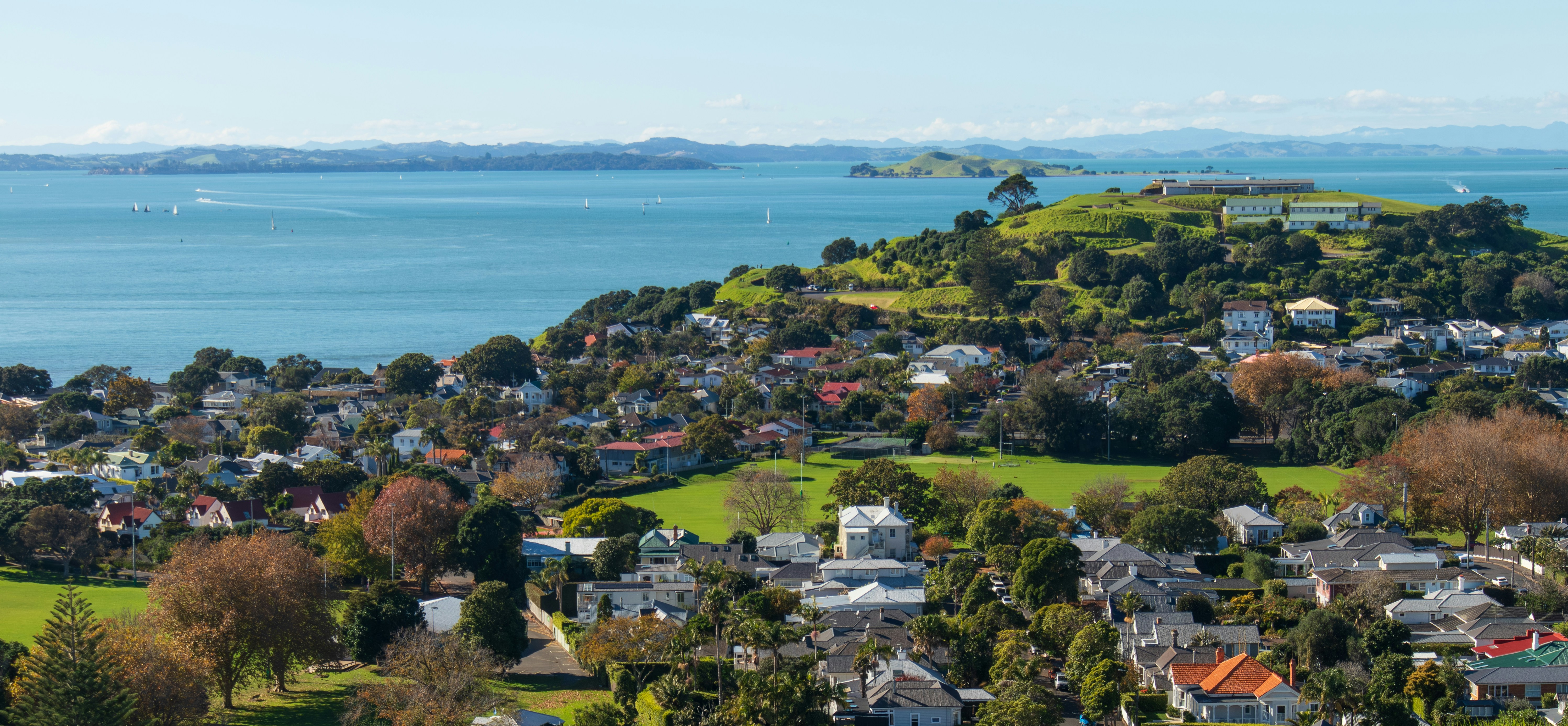 A coastal town with houses and green parks overlooking a blue bay
