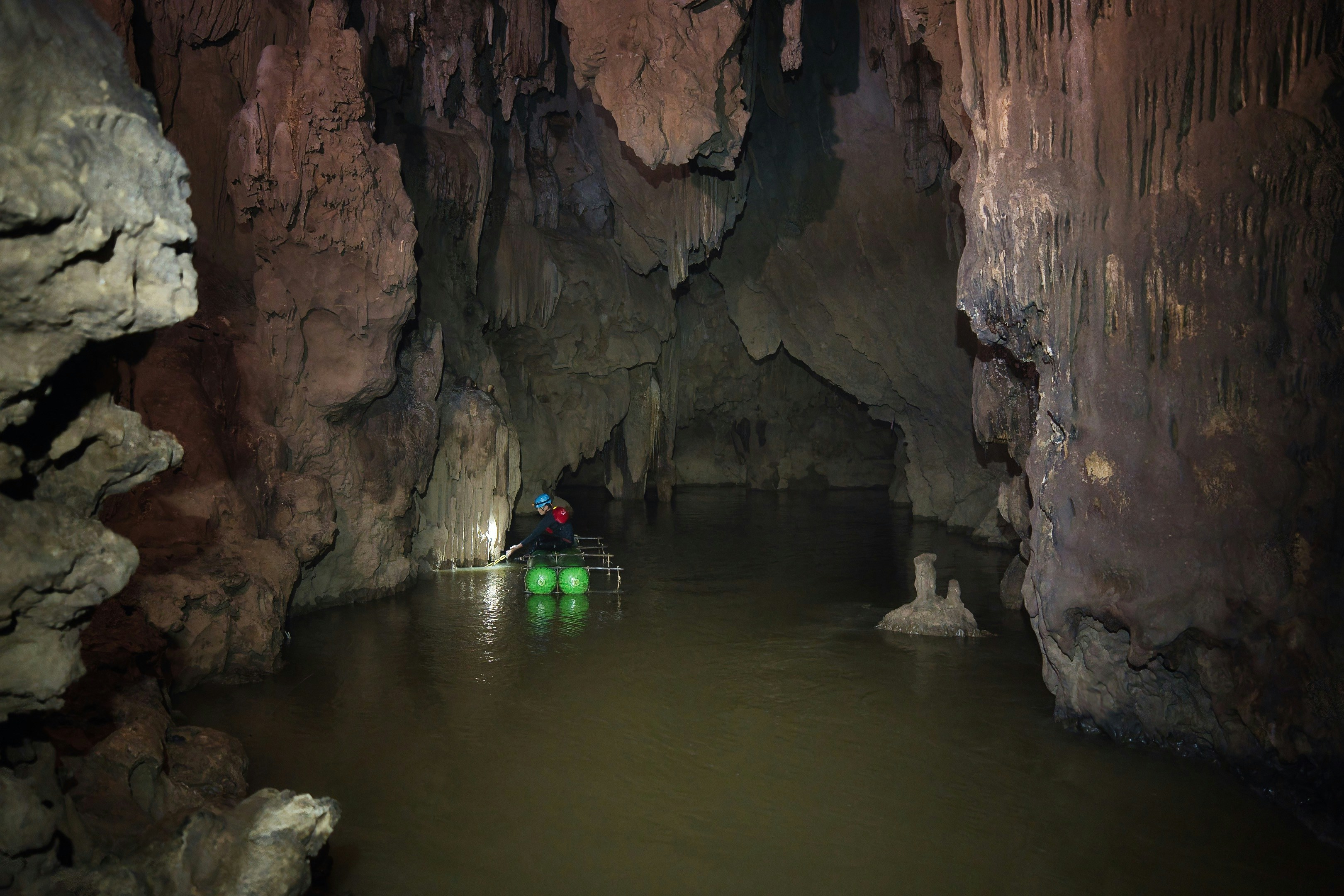 A person in a blue helmet paddling a small raft through a dark cave