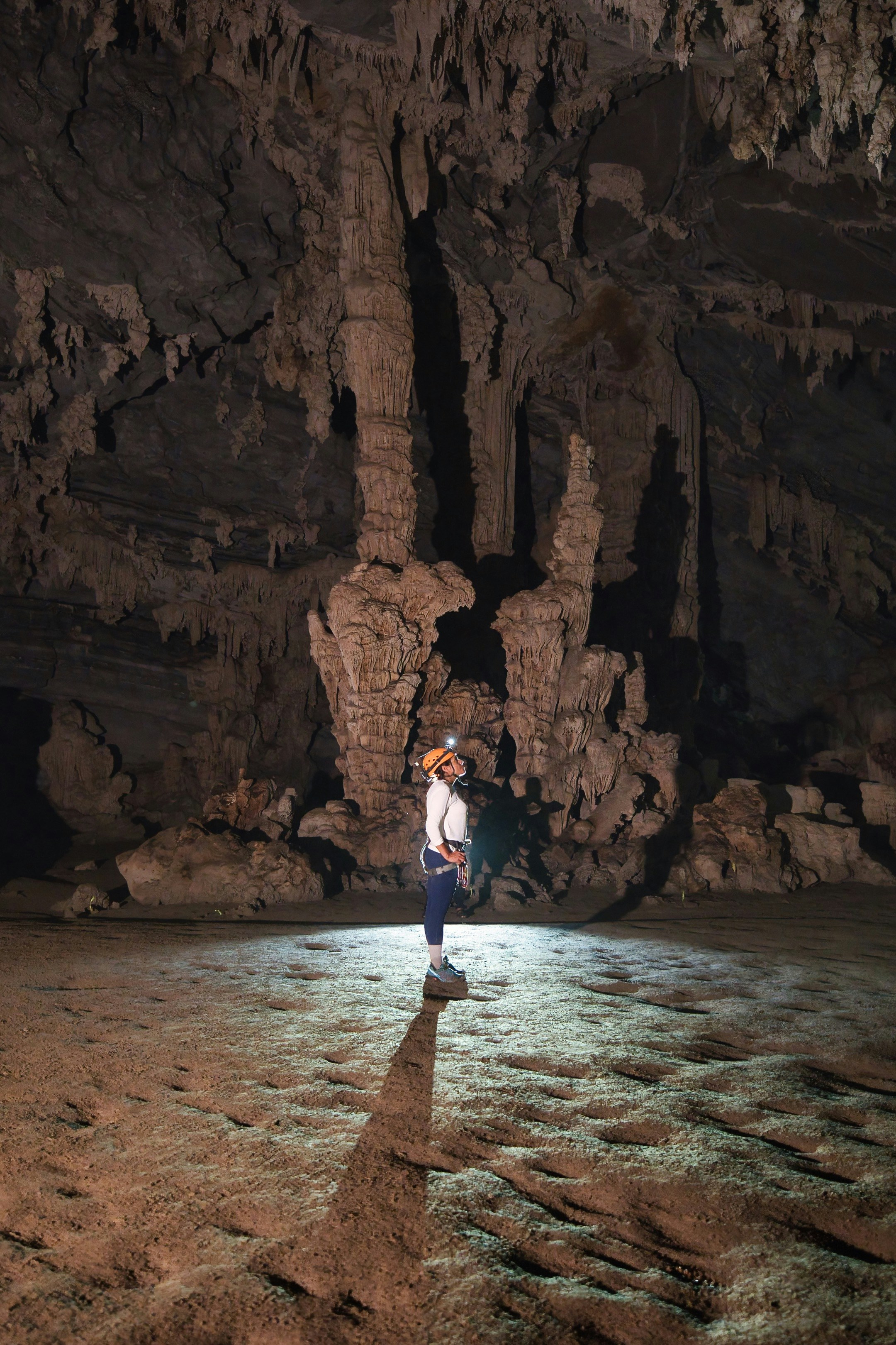 A person in a helmet and harness exploring a large cave with rock formations