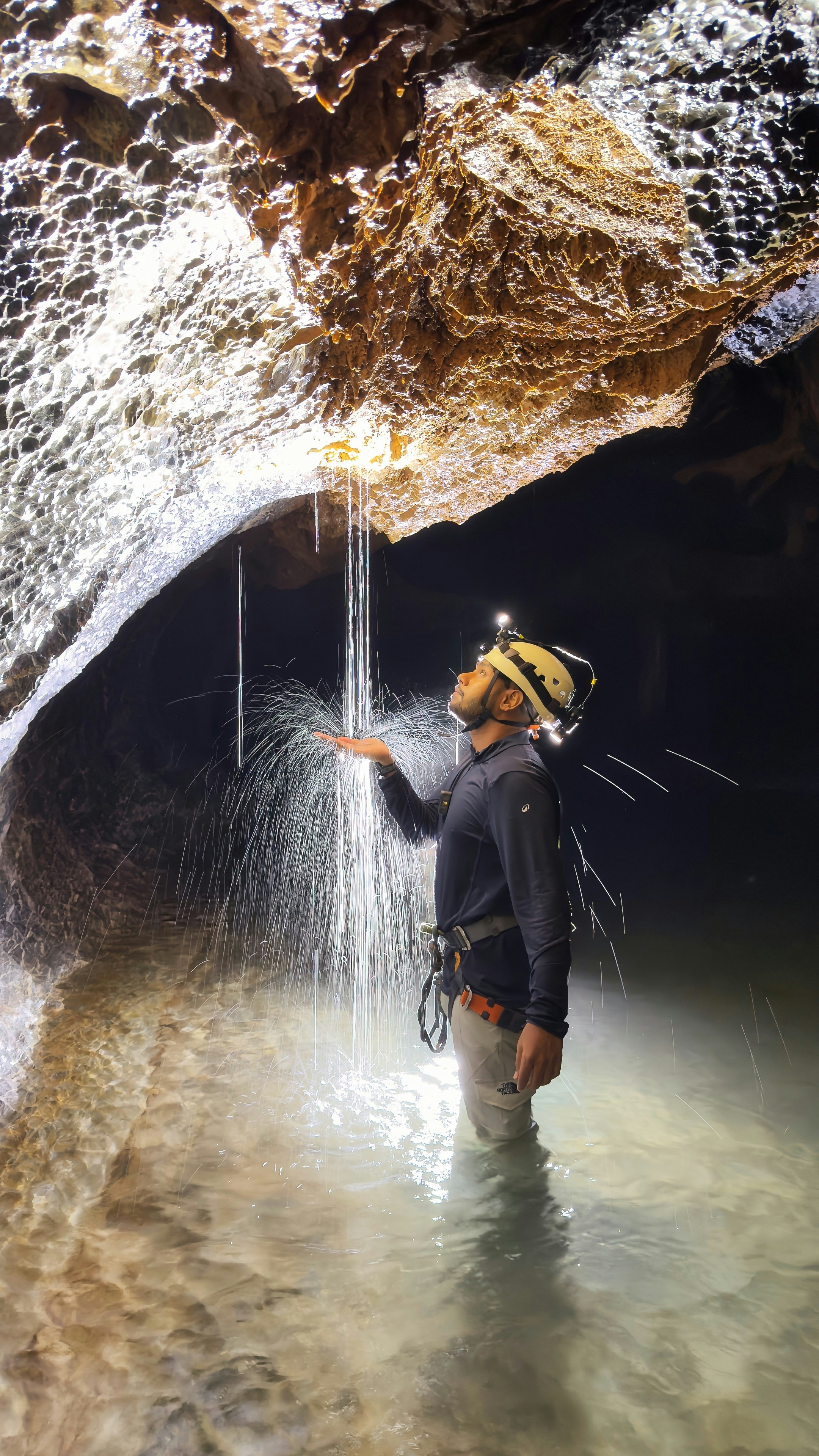 A person in a helmet and headlamp catching water dripping from a cave ceiling