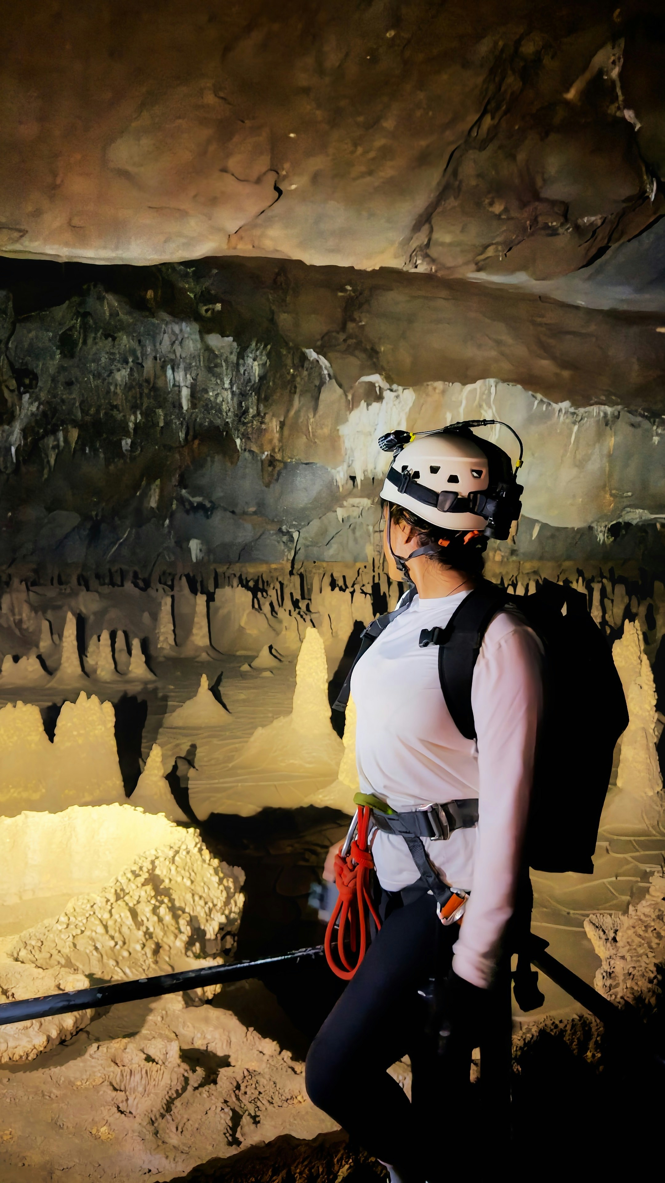 A person in a helmet and harness exploring a cave with illuminated stalagmites
