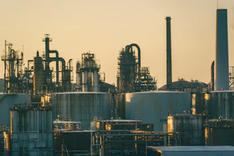 Industrial refinery with storage tanks and metal pipes under a warm golden sky