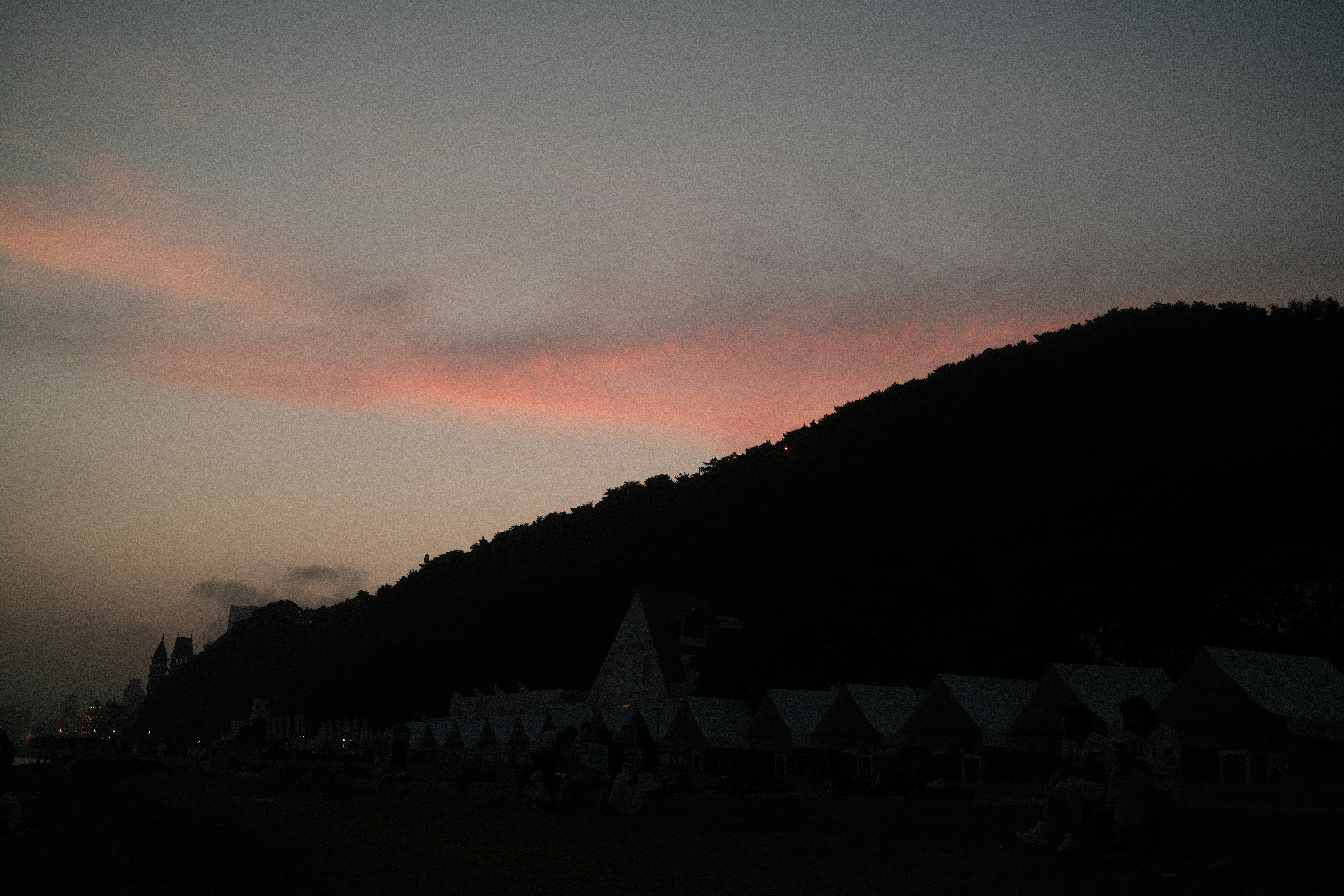 A dark hillside silhouette against a sky with soft pink clouds