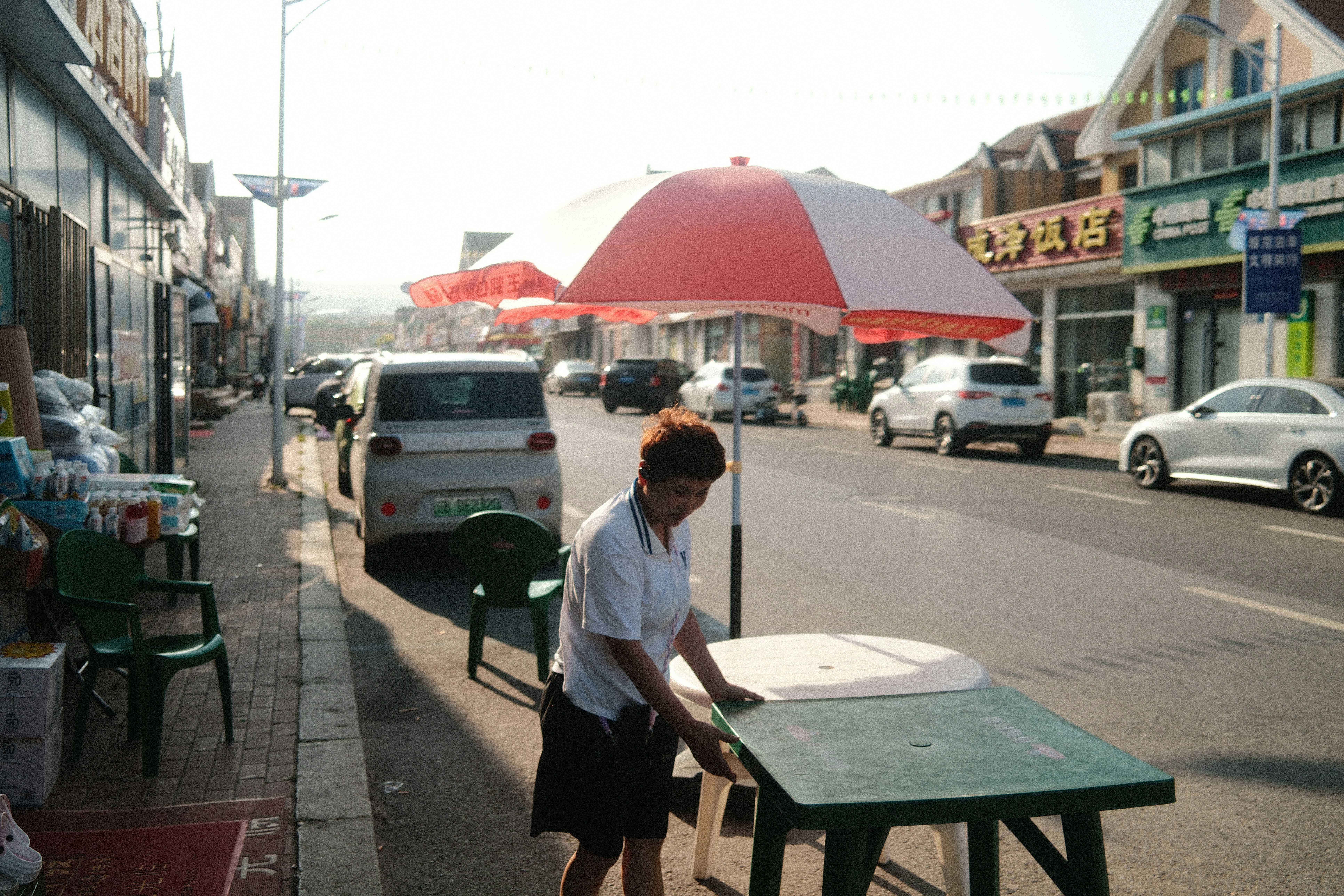 A person setting up a green table under a red and white umbrella