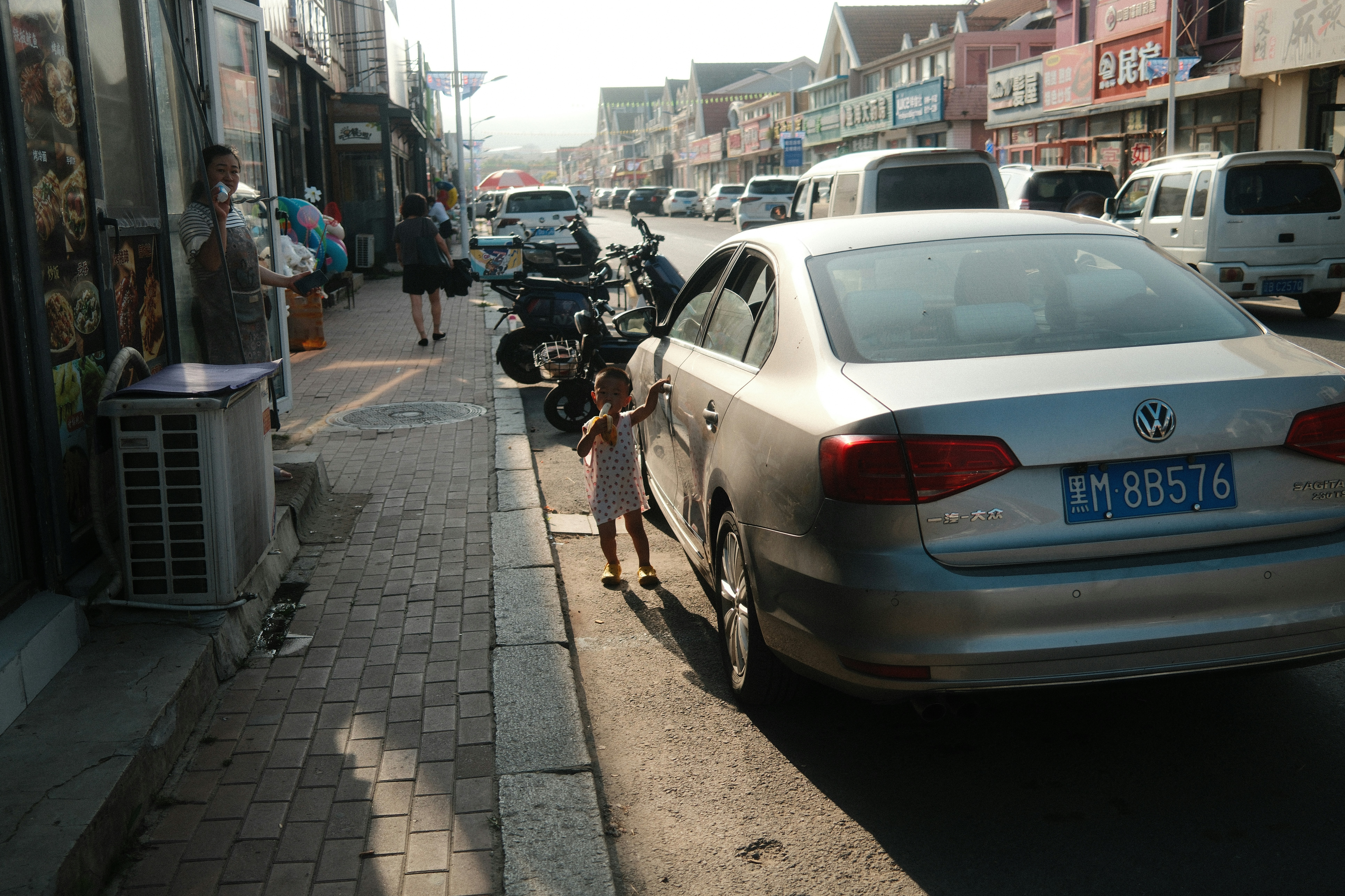 A child standing beside a silver car on a paved city street