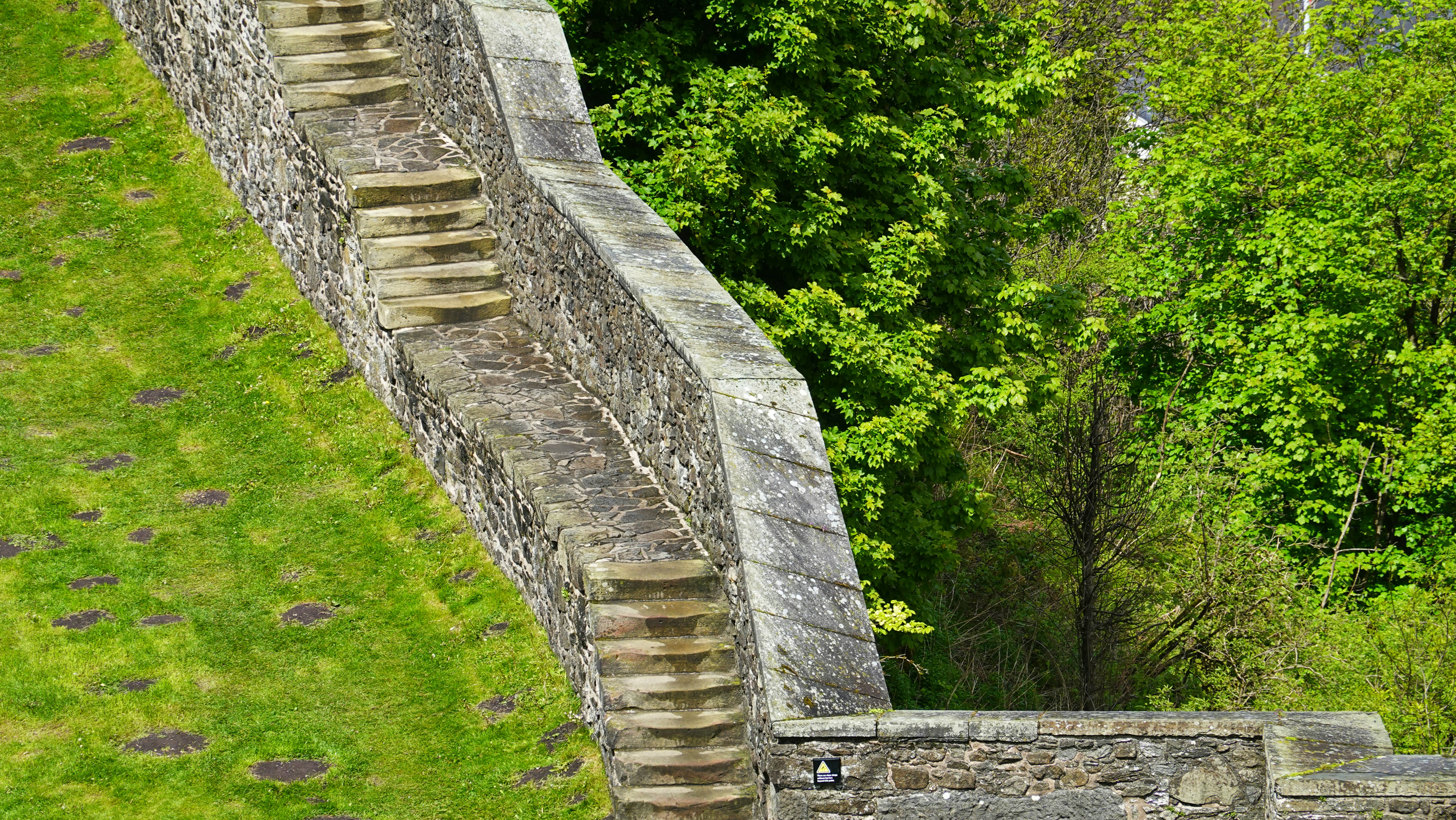 Stone stairs built into a high retaining wall beside a green grassy slope