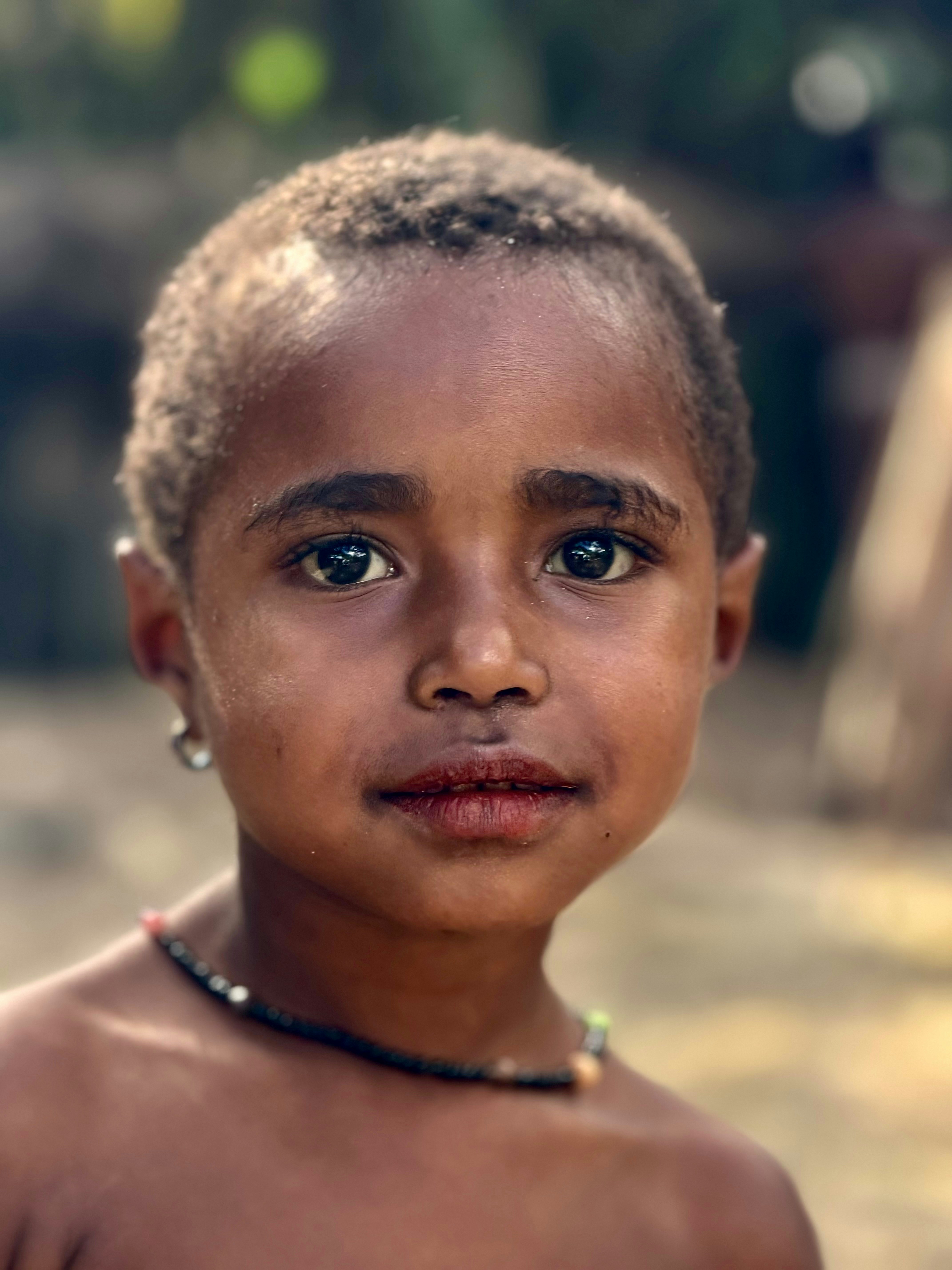 A child with short hair wearing a beaded necklace and a small silver earring