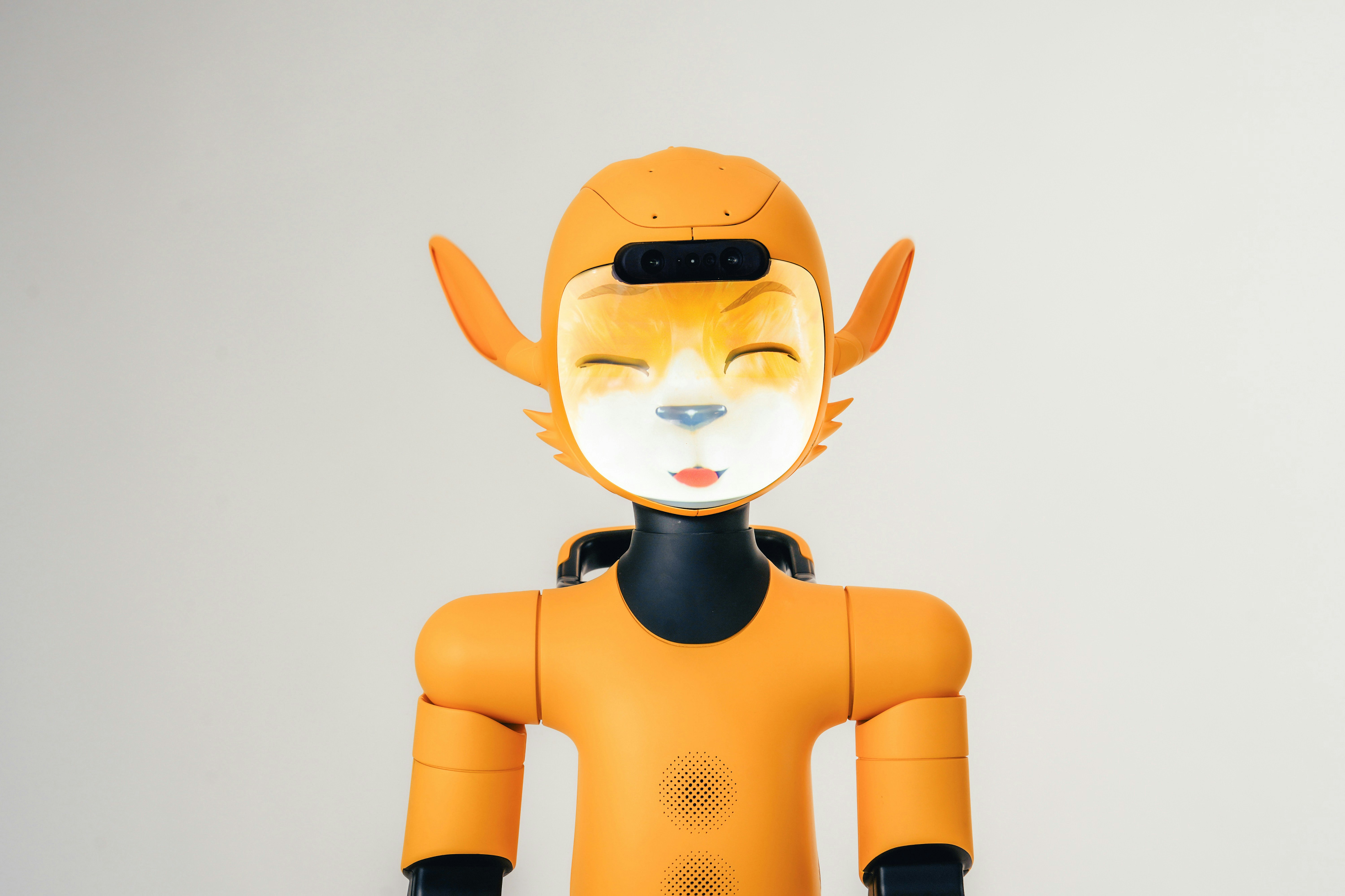 An orange robot with a digital screen face displaying a stylized animal expression