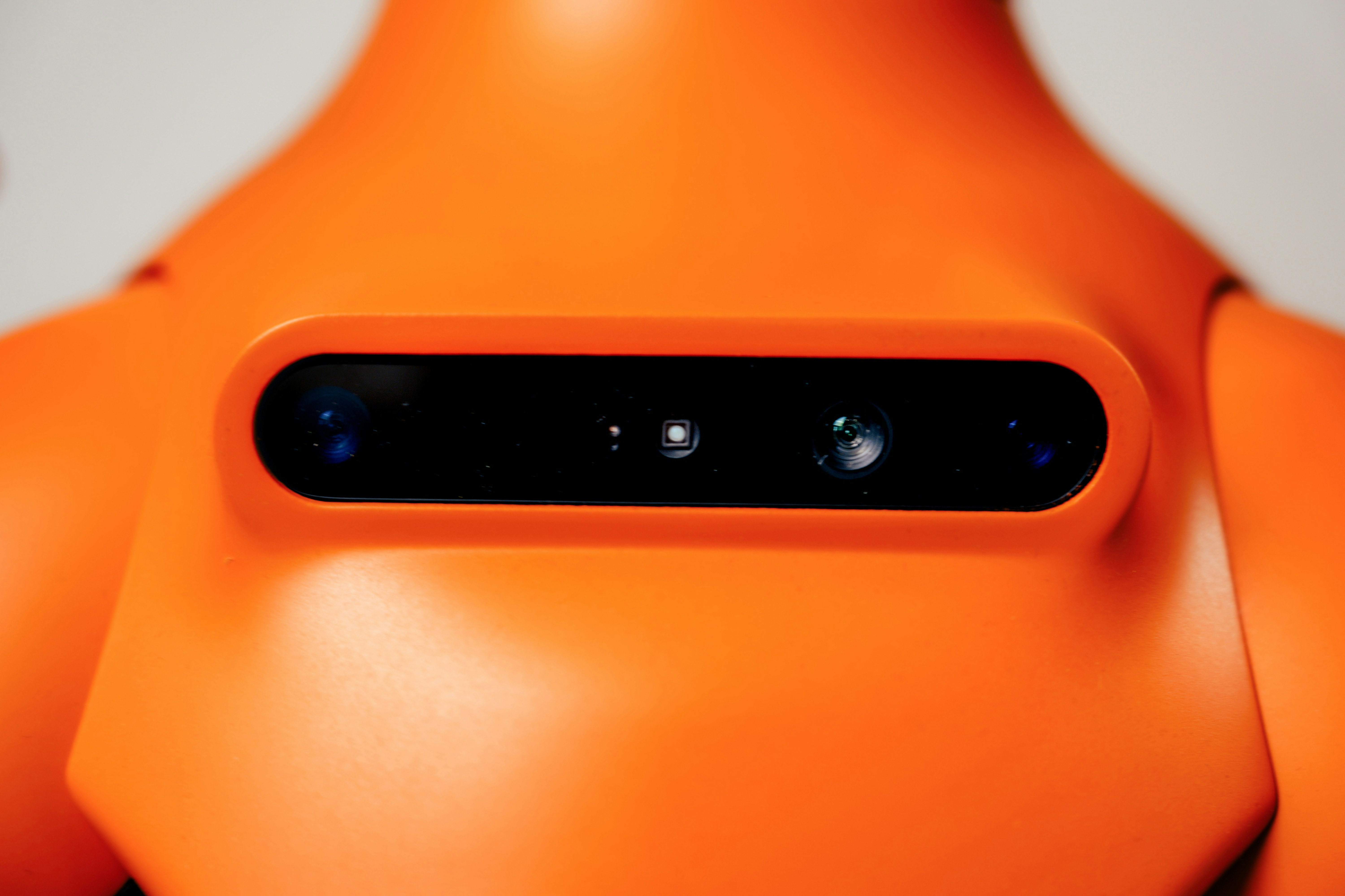A close-up of a bright orange robot head with two camera lenses