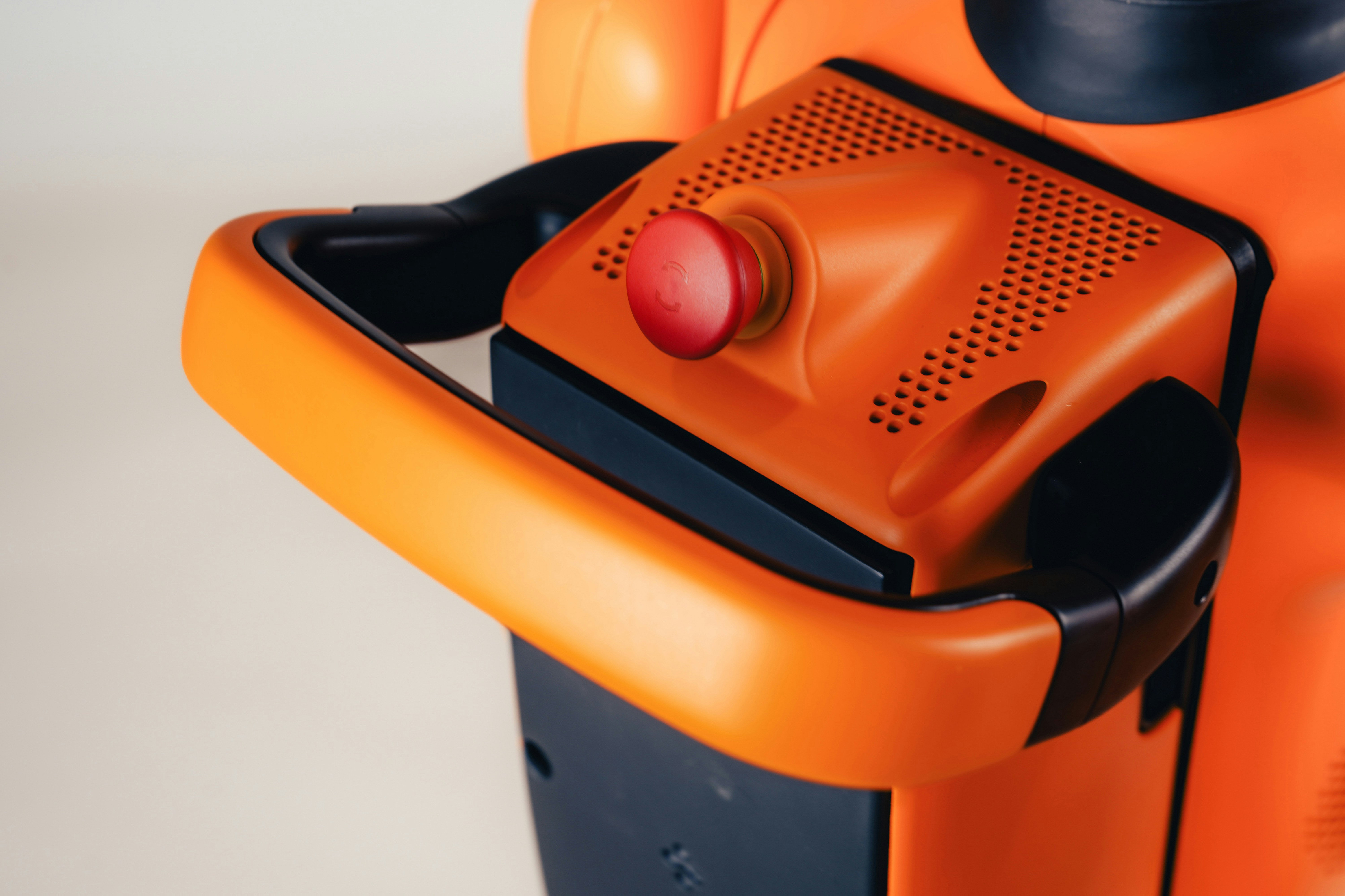 A bright red emergency stop button on an orange industrial machine handle