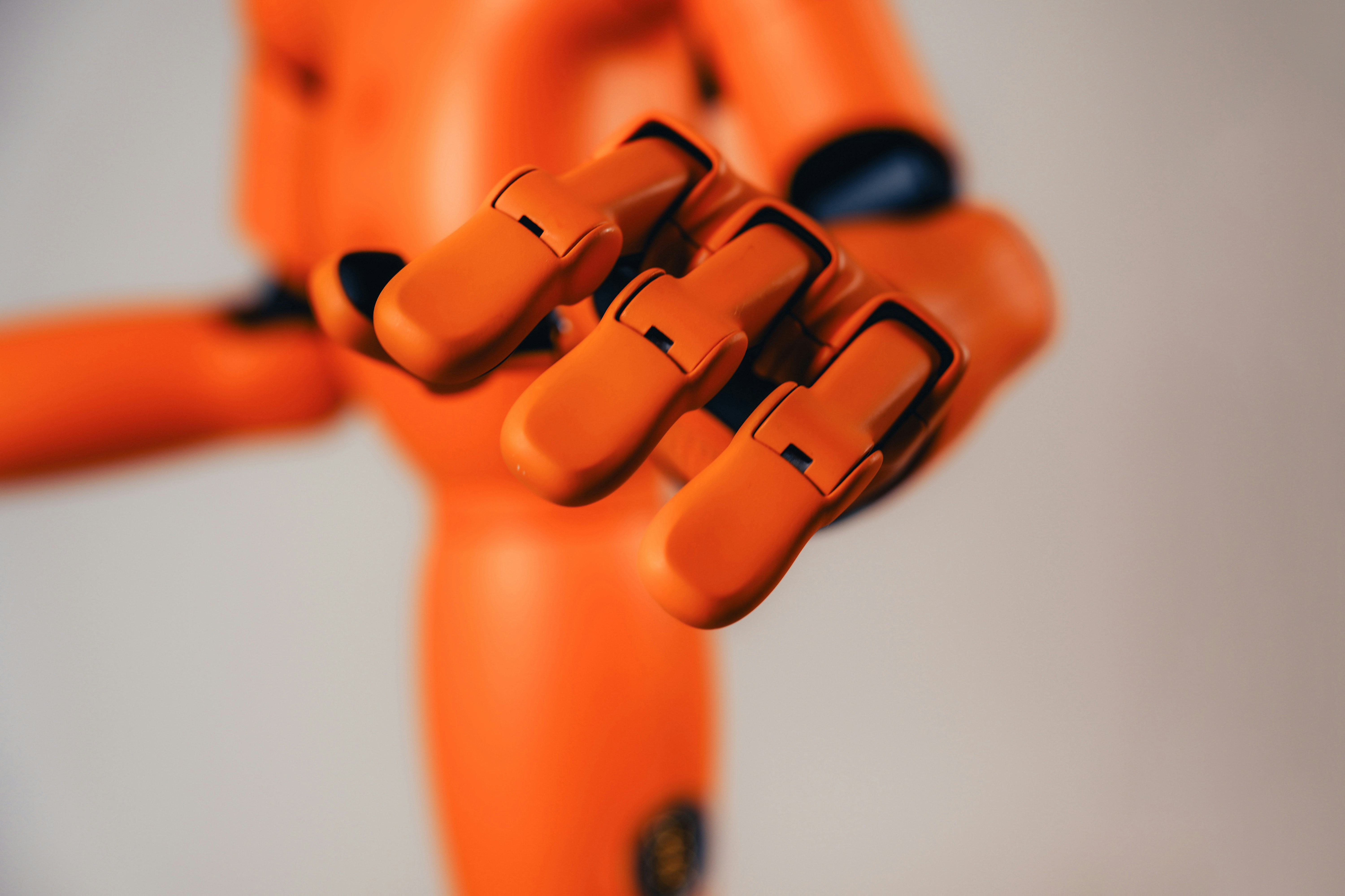 A bright orange robotic hand reaching forward against a plain light background