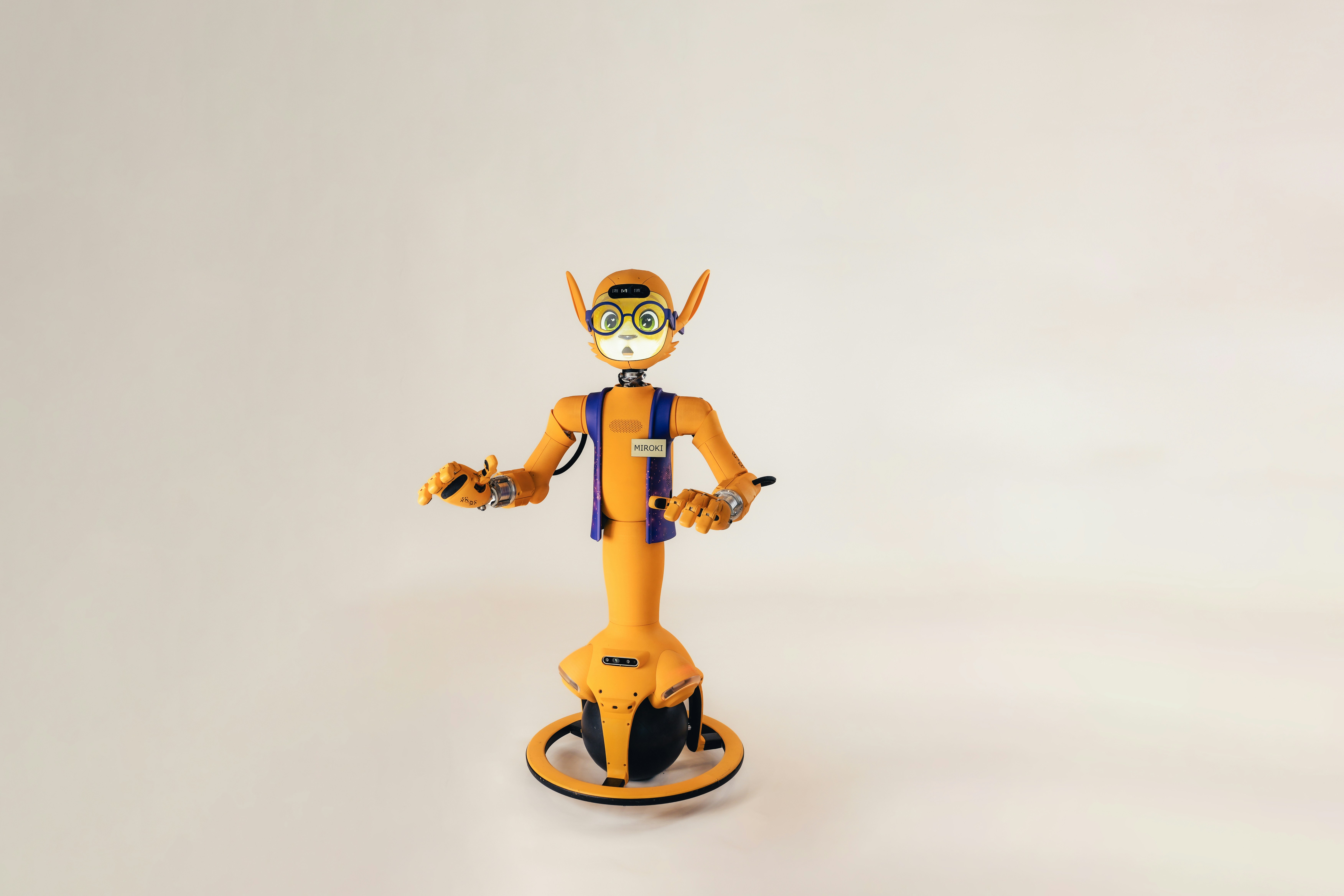 An orange robot with large ears and glasses on a single wheel base
