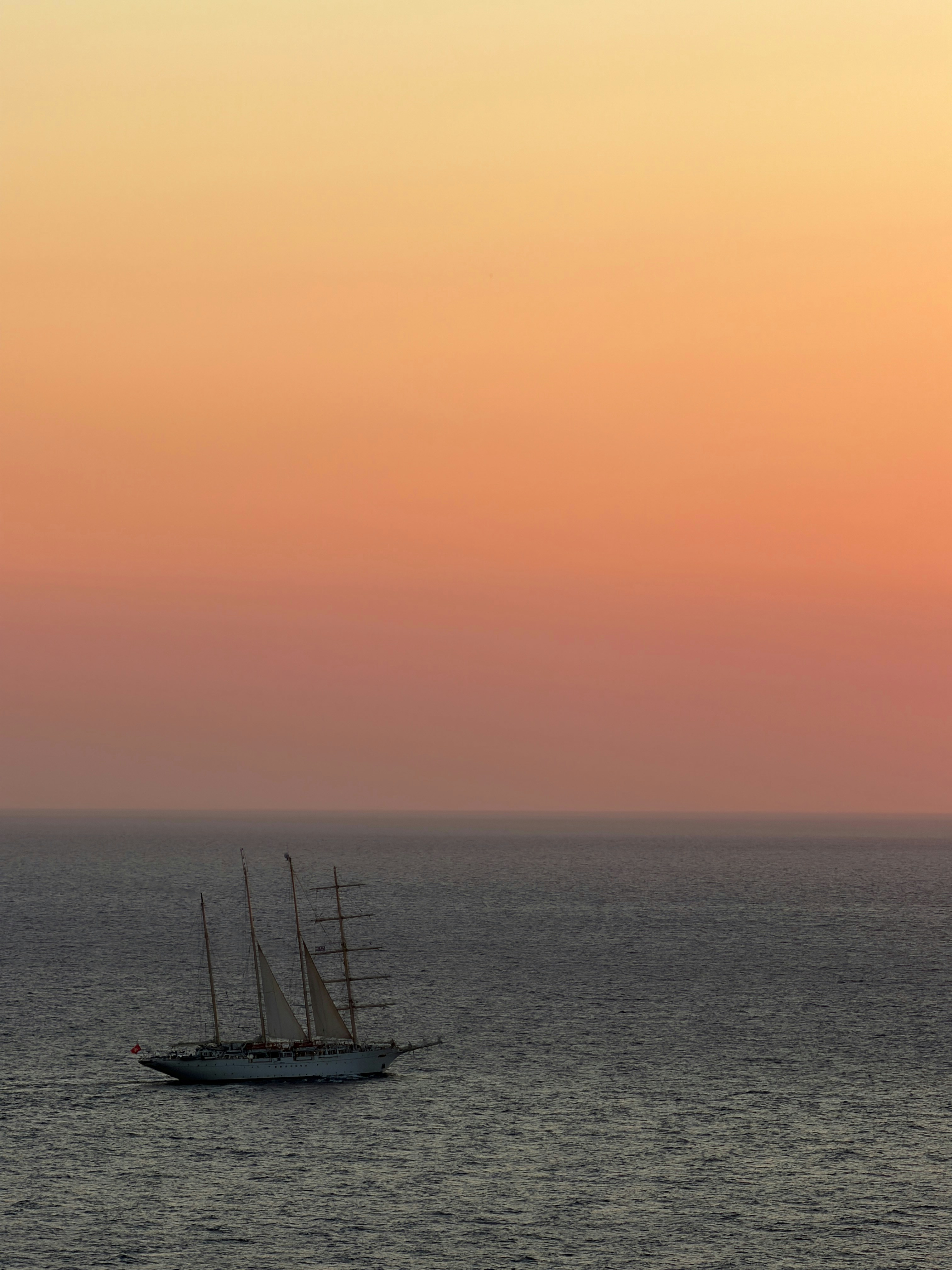 A tall ship sailing on the open sea under a warm orange sky