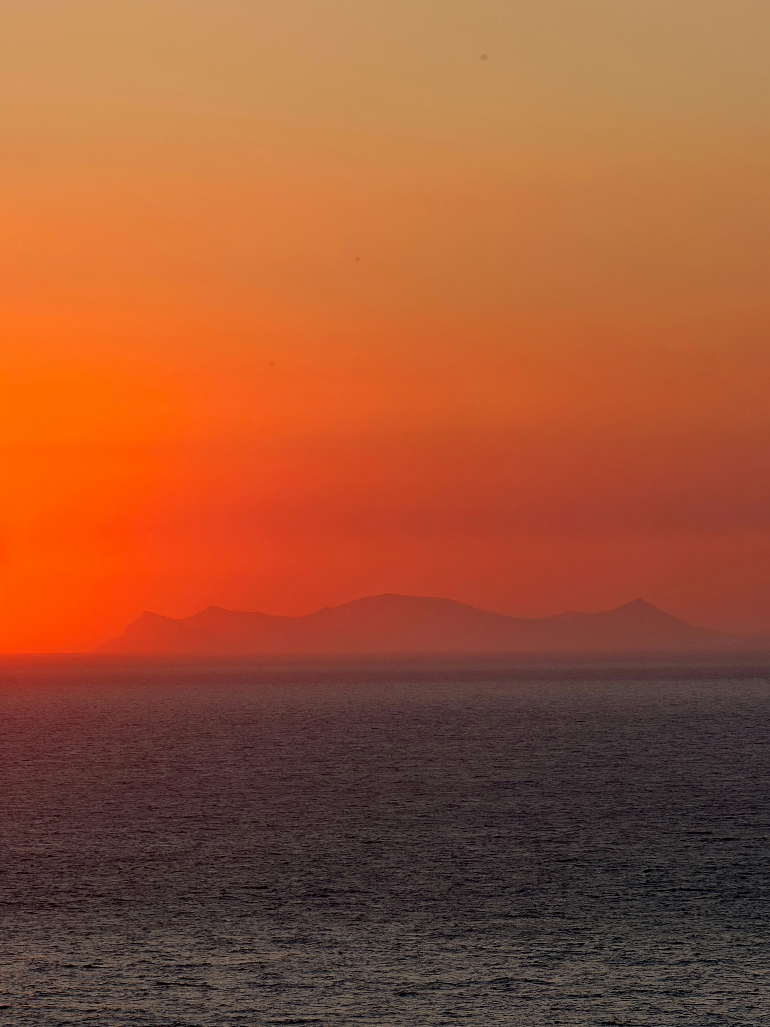 A distant island silhouette against a vibrant orange sky above the dark ocean