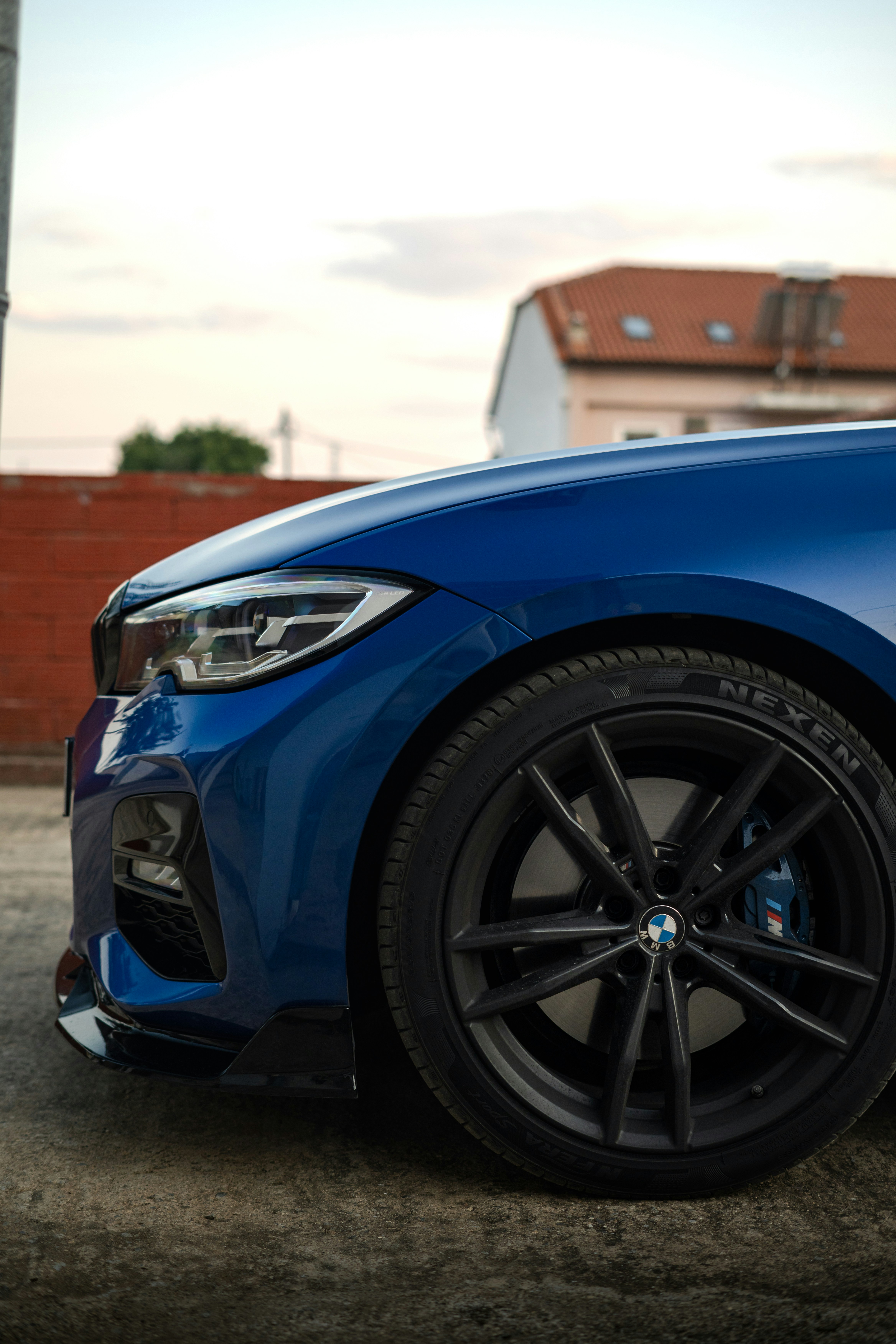 Un coche azul con ruedas negras aparcado sobre una superficie de hormigón al anochecer
