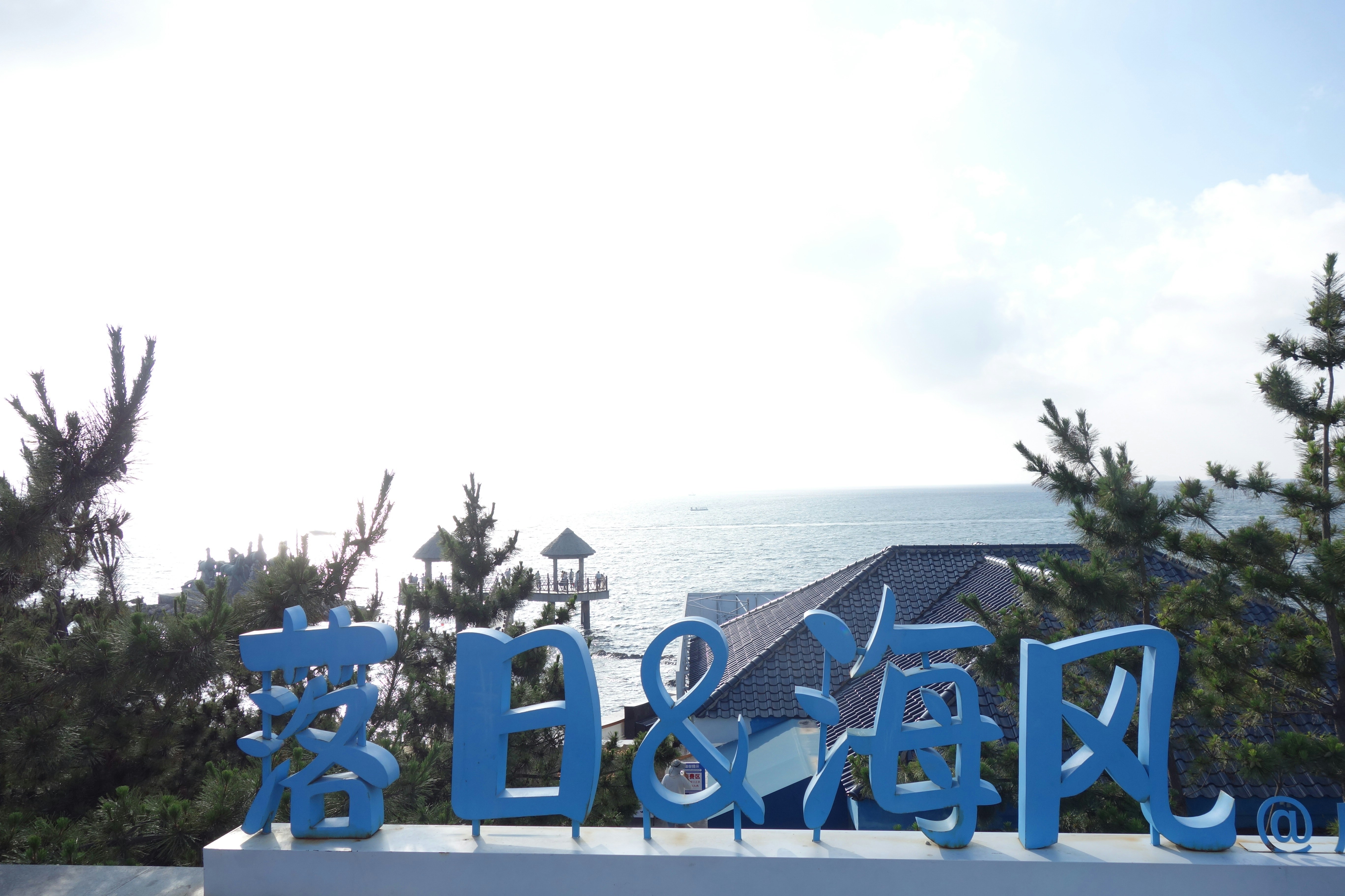 Blue Chinese characters on a sign overlooking a coastal sea view with pavilions