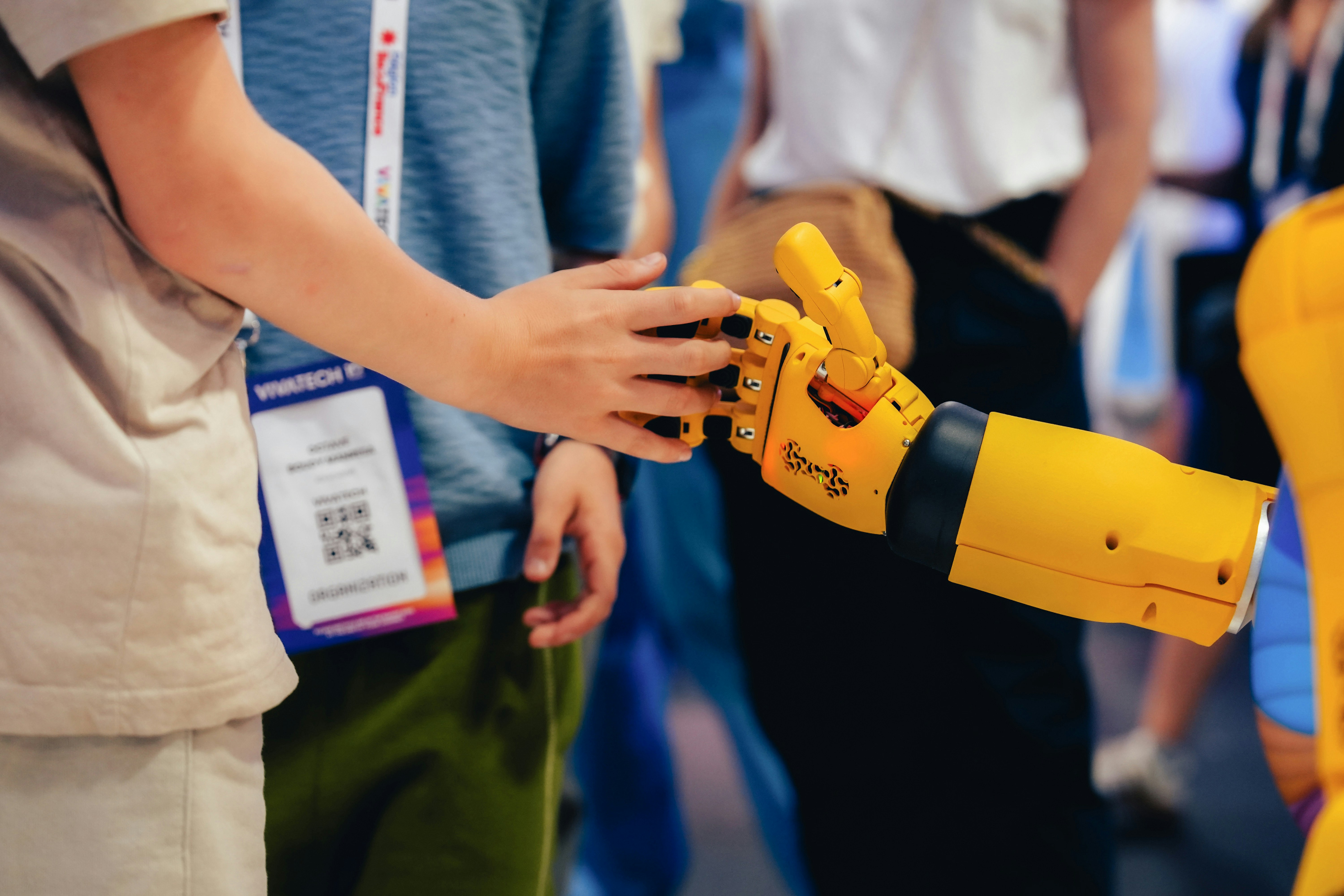 A person touching the yellow robotic hand of a machine at a conference