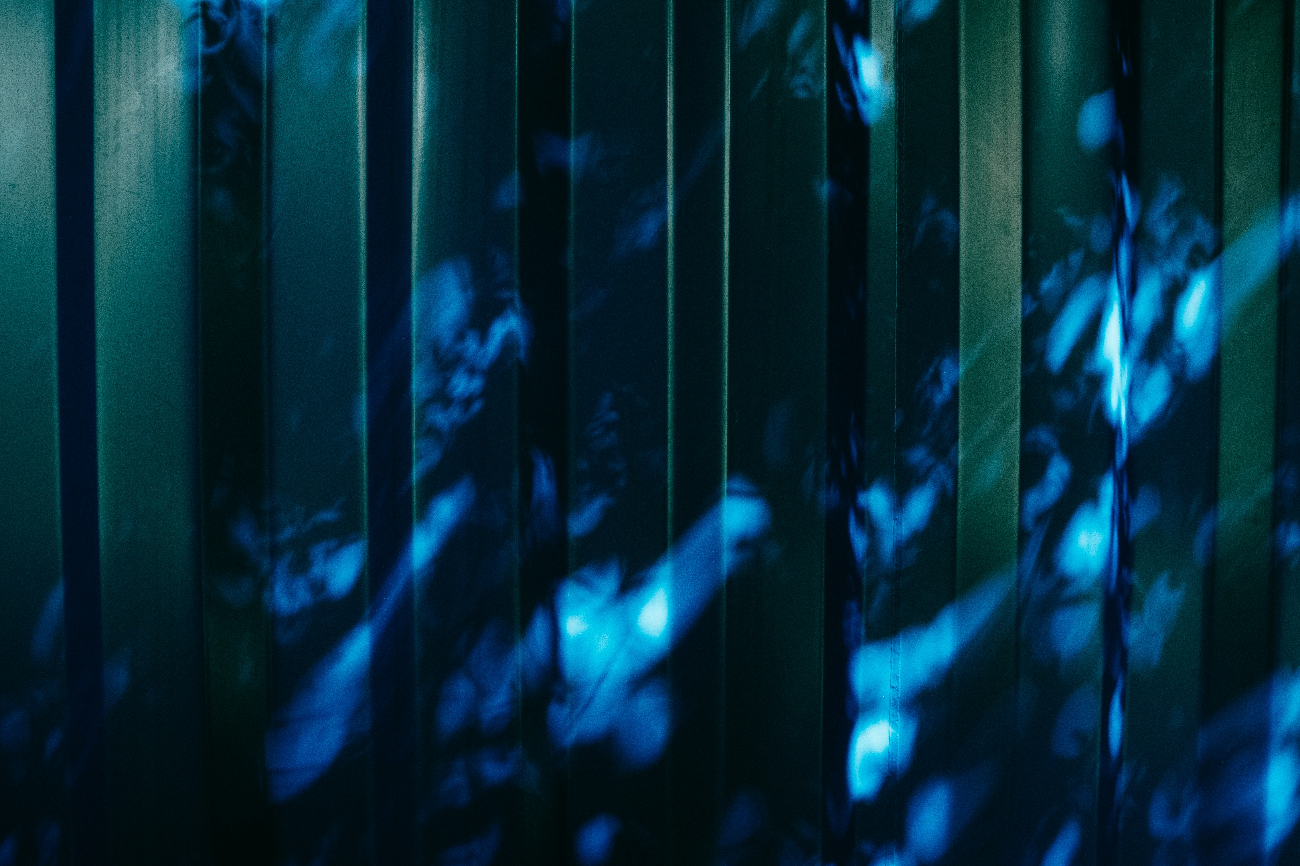 Padrões de luz azul projetados sobre uma superfície de metal ondulado verde-escuro