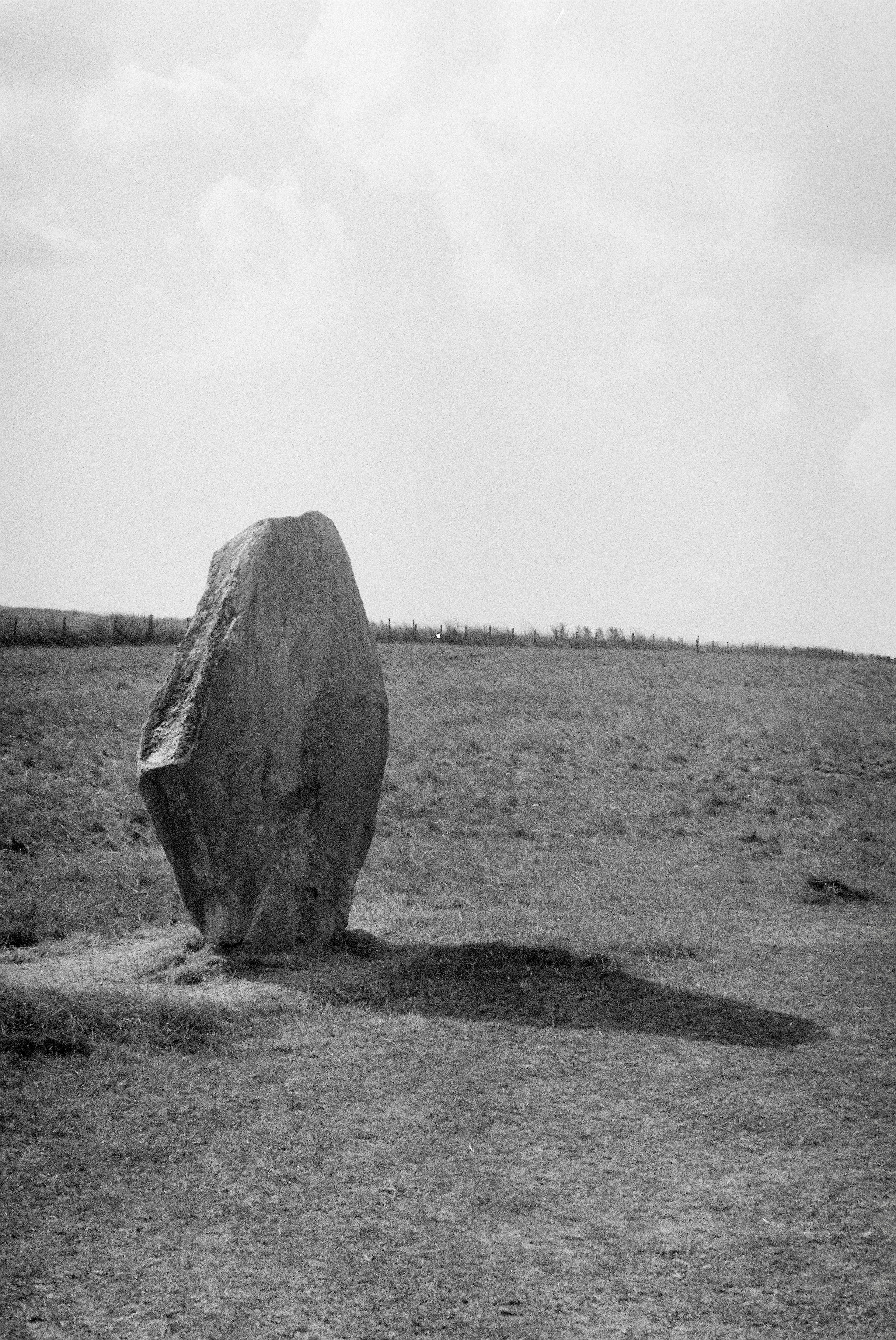 A large standing stone in a grassy field under a bright sky