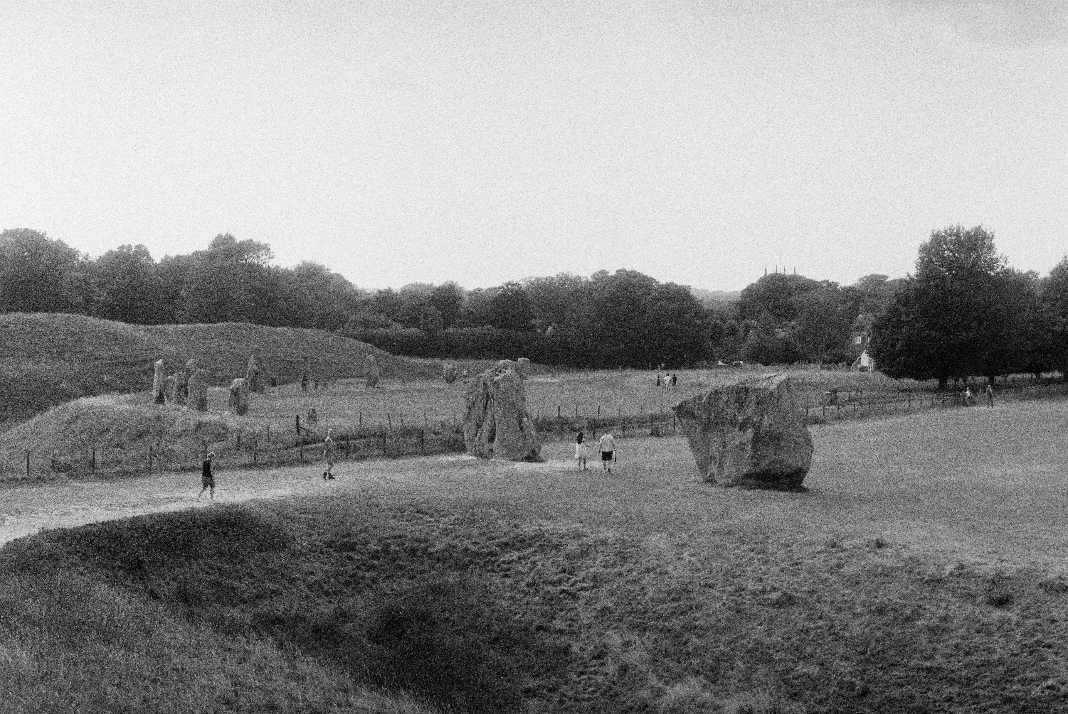 People walking past large standing stones in a grassy field at Avebury