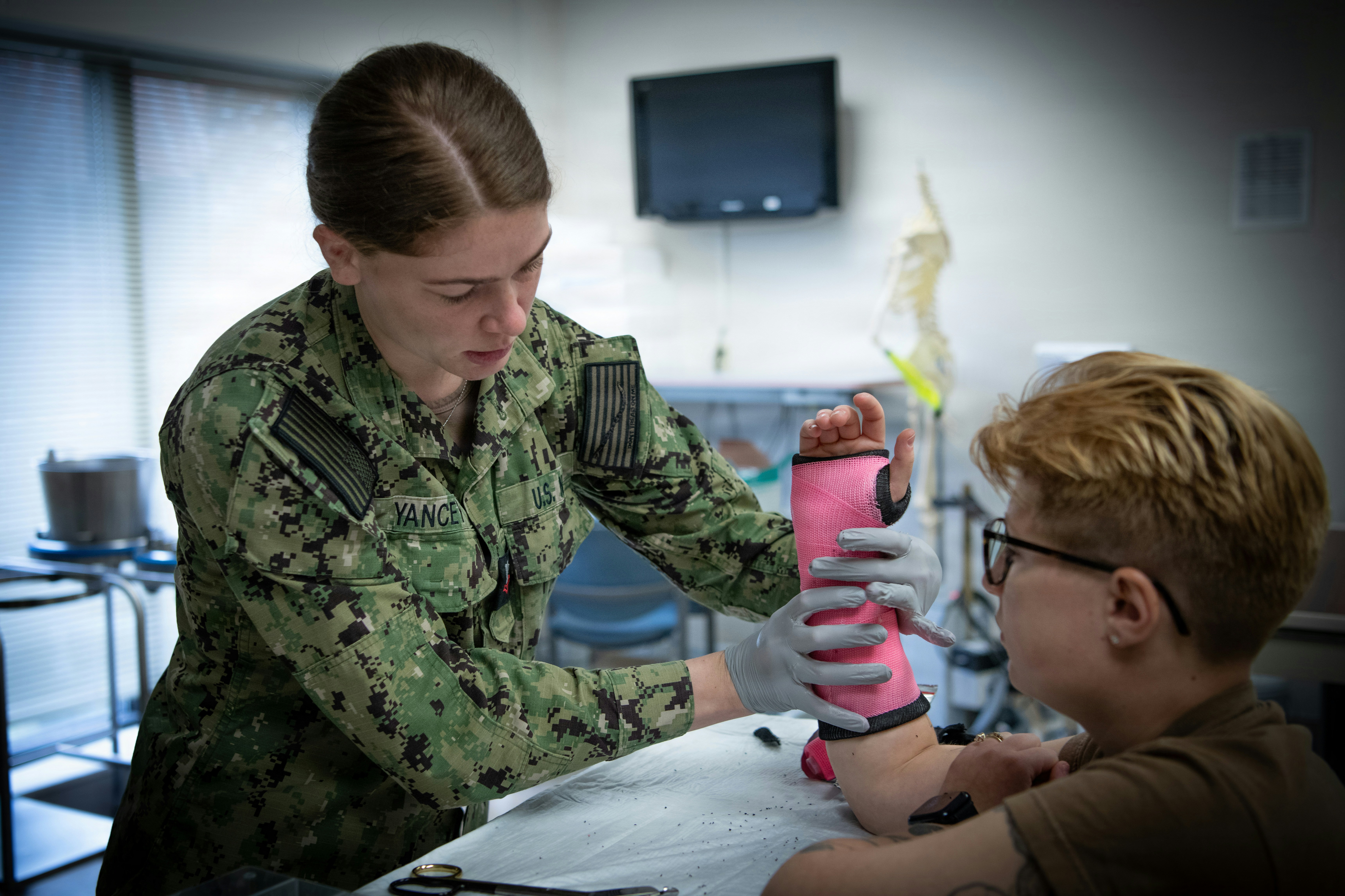 A person in a military uniform adjusting a pink cast on a patient's arm.