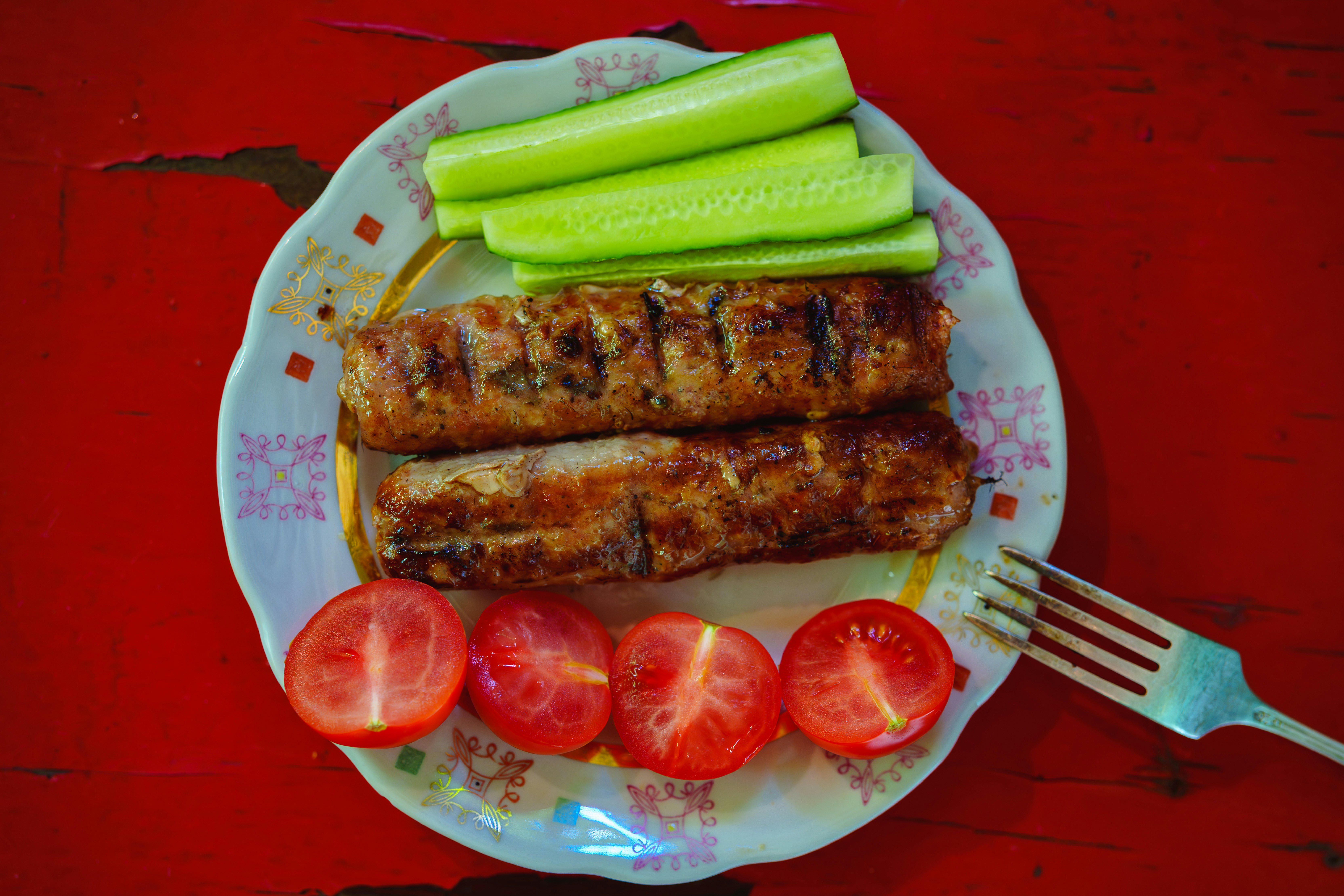 Deux saucisses grillées avec des tranches de concombre et des tomates cerises coupées en deux sur une assiette