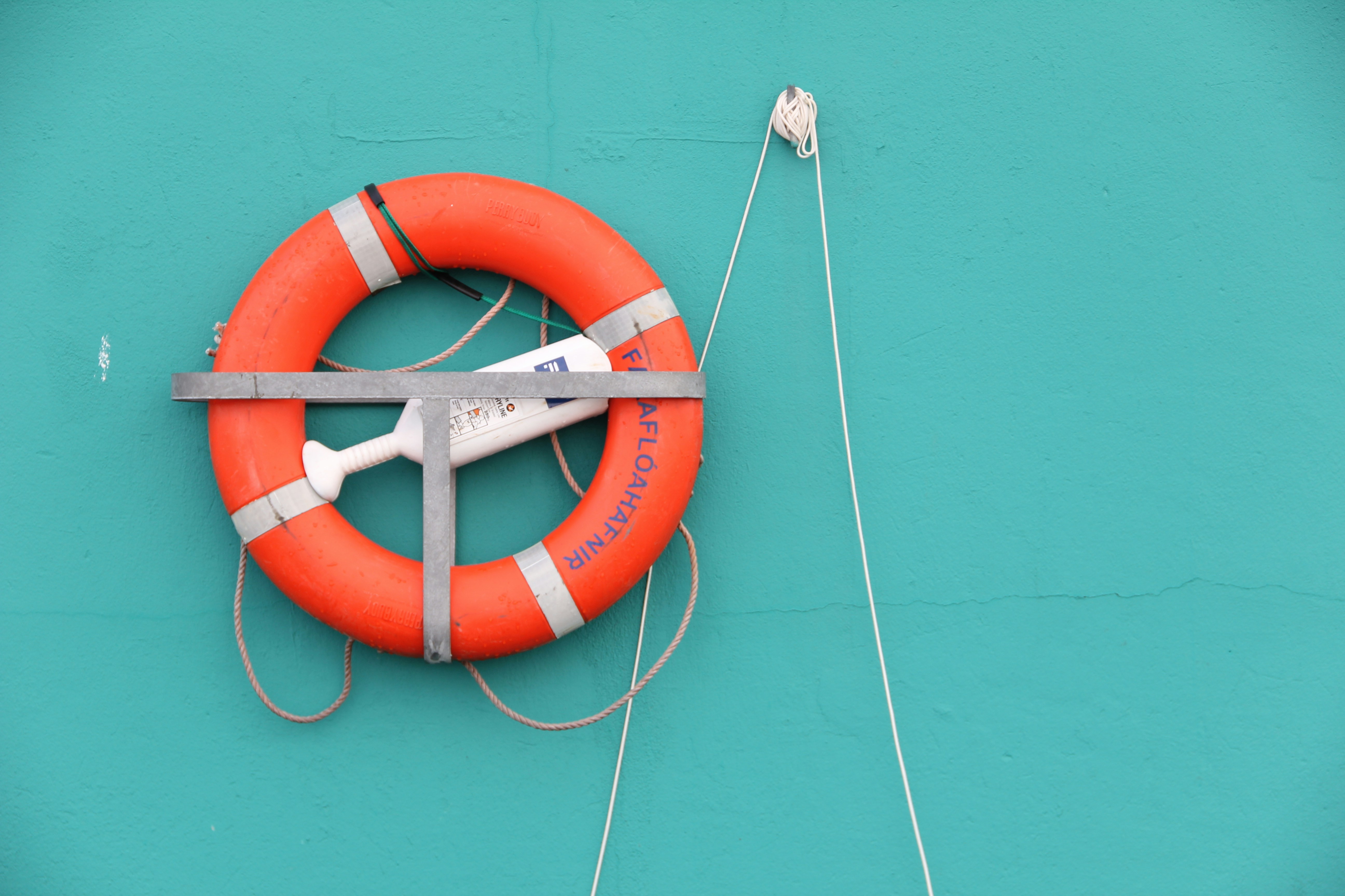 An orange lifebuoy mounted on a vibrant teal wall with a white rope