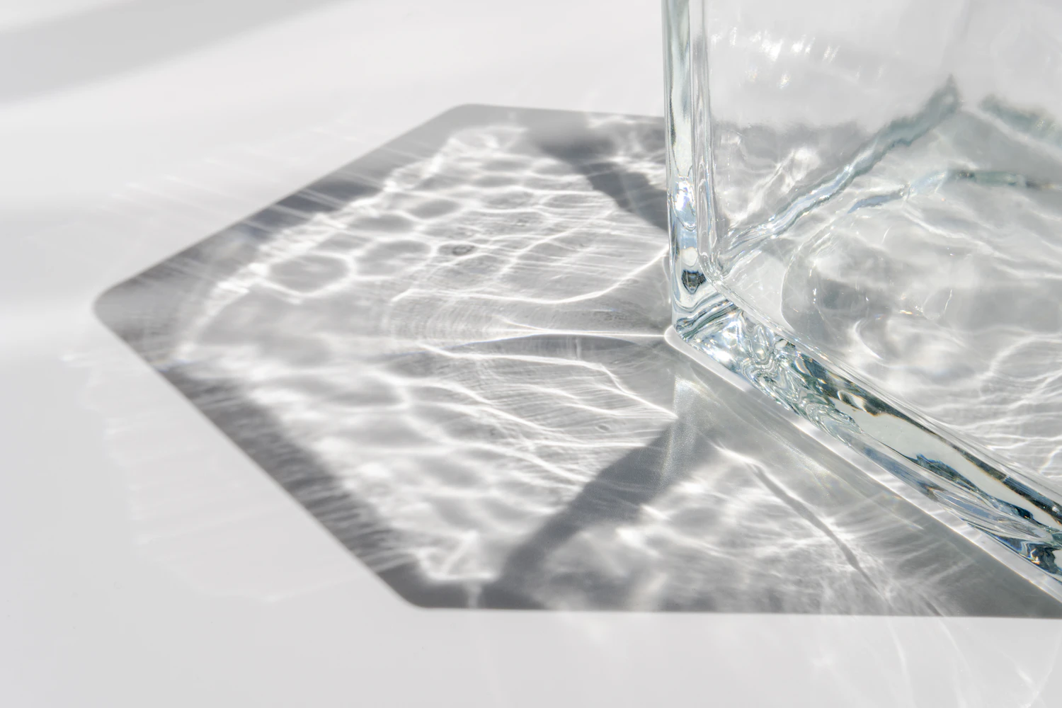 Sunlight passing through a thick glass vessel and rippling across a white surface