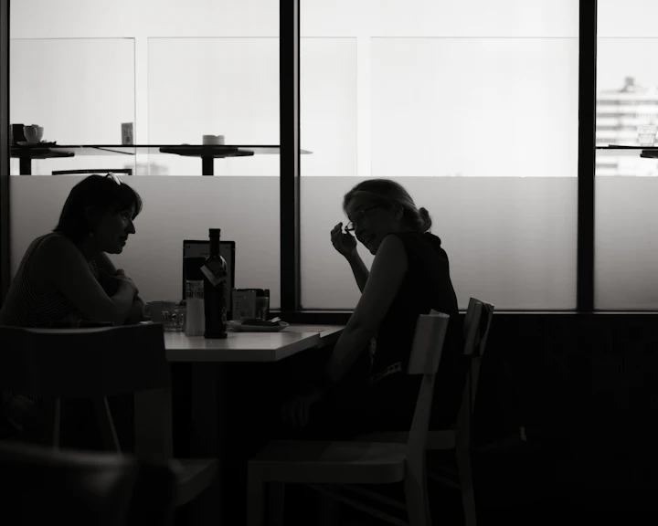 Two people in silhouette at a table in a bright cafe