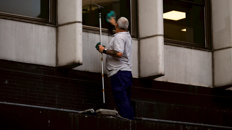 A maintenance worker using an extended squeegee to clean the exterior windows of a commercial building