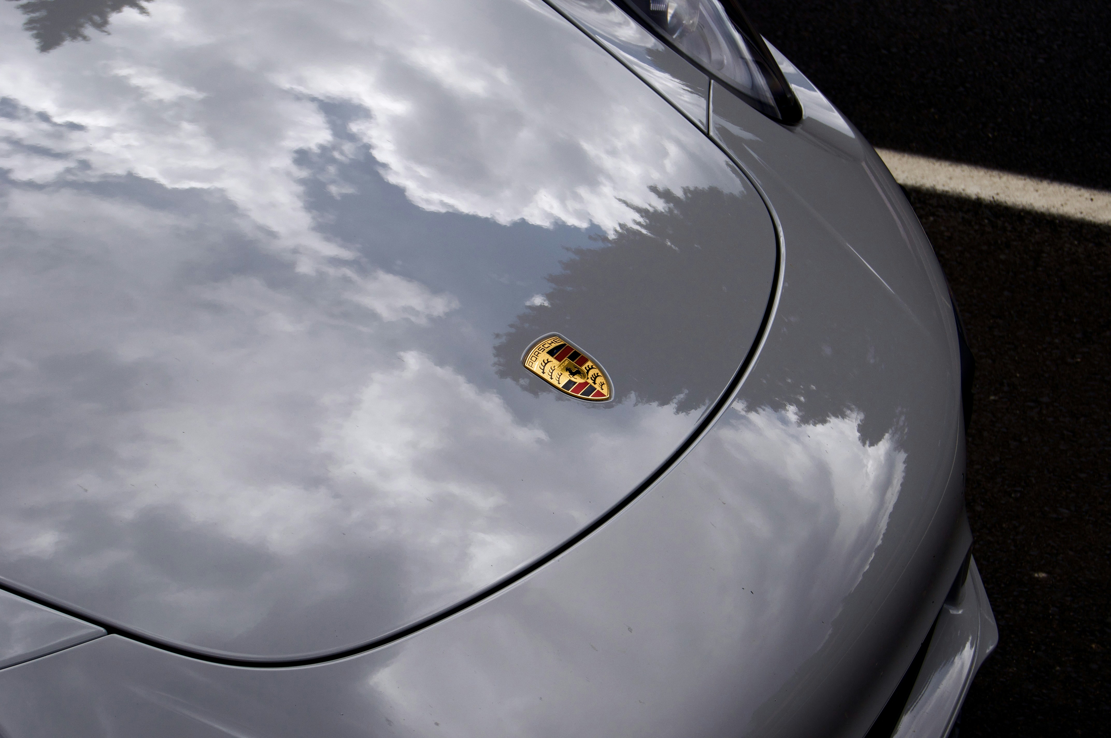 A grey car hood reflecting clouds and trees with a Porsche emblem