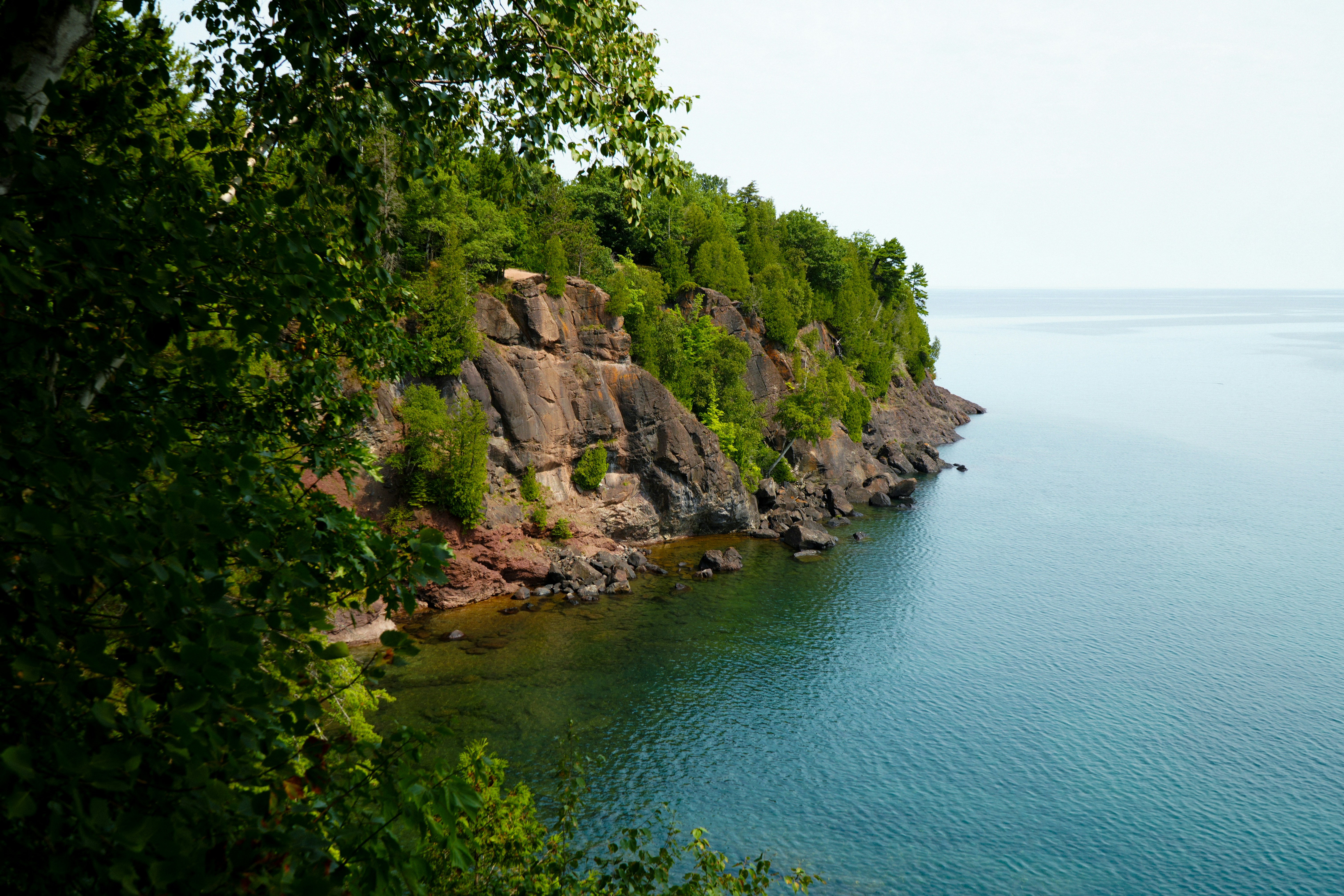 Marquette to Copper Harbor on the Keweenaw – A rocky cliff covered in green trees overlooking calm blue water