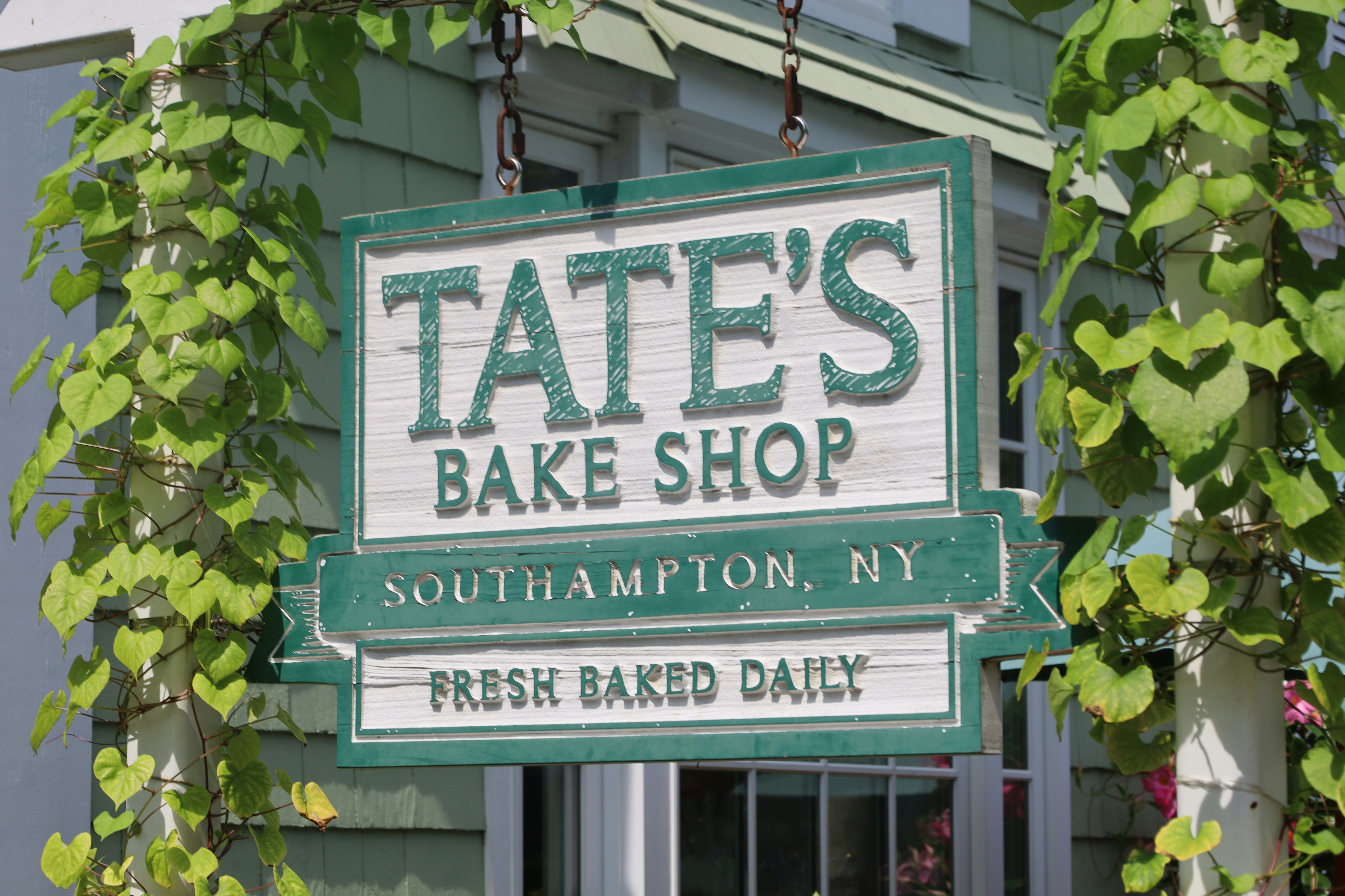 A wooden sign for Tate's Bake Shop in Southampton, NY, framed by green vines