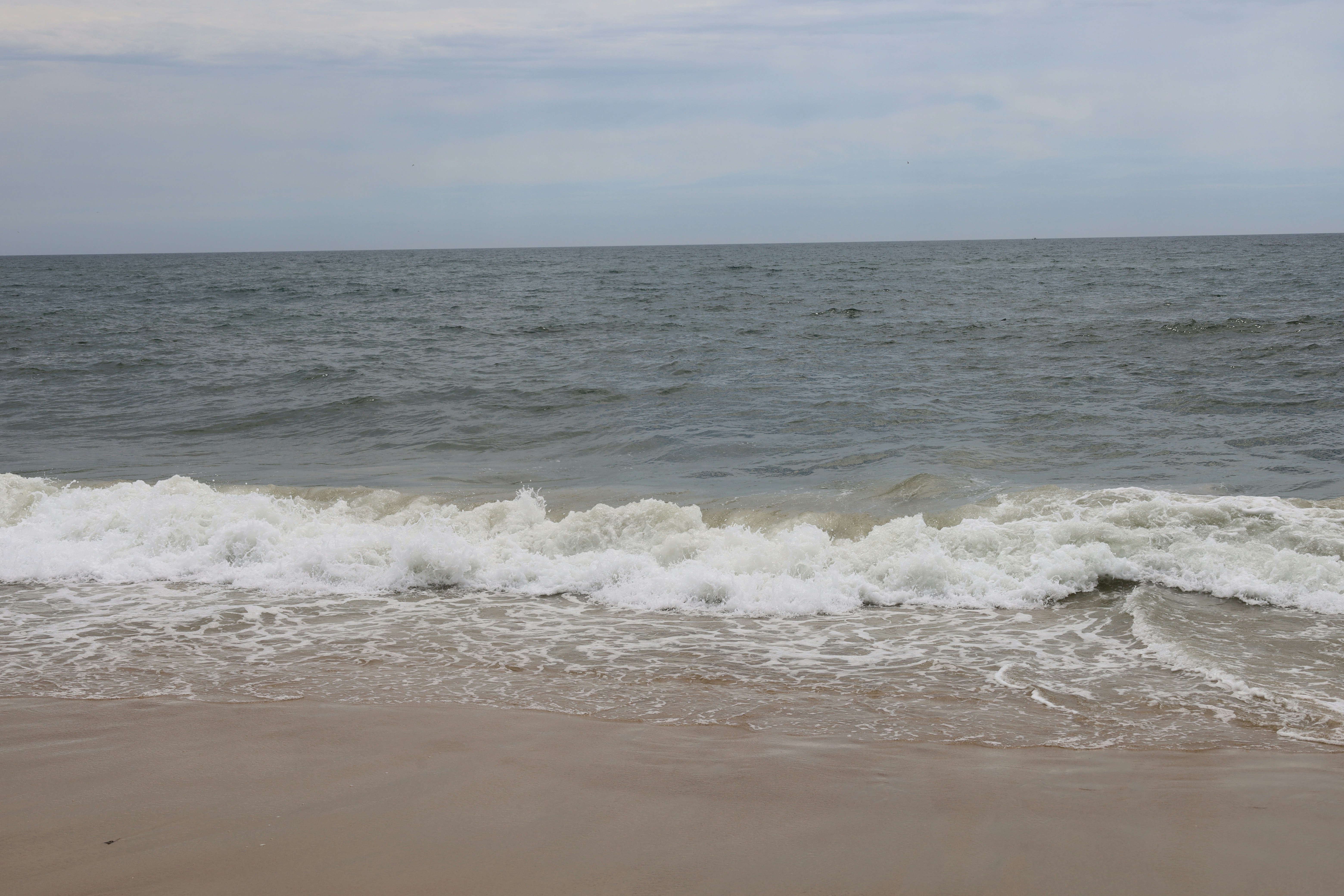A white wave breaking on a sandy beach under a cloudy sky