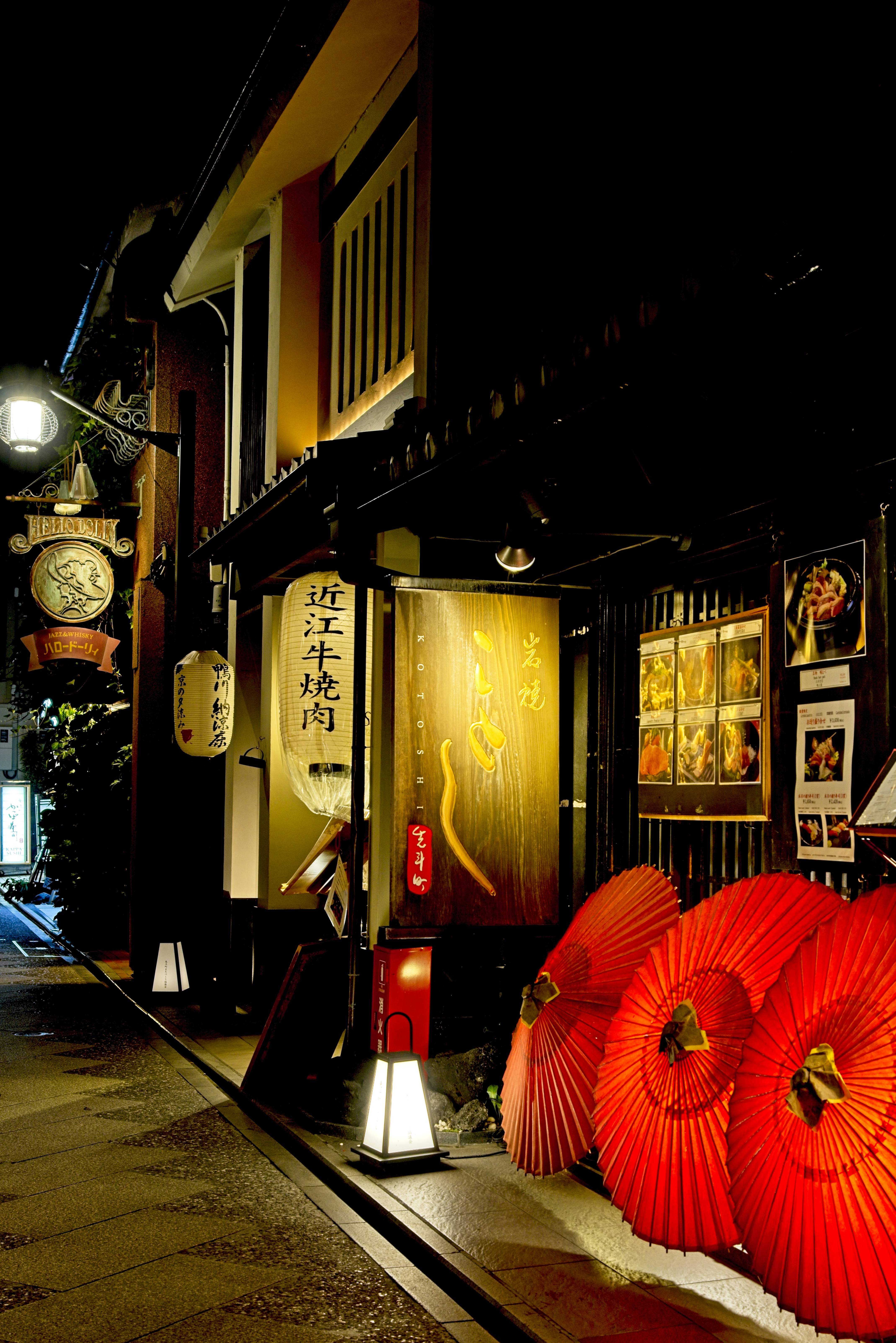 Red paper umbrellas outside a restaurant with glowing lanterns on a dark street